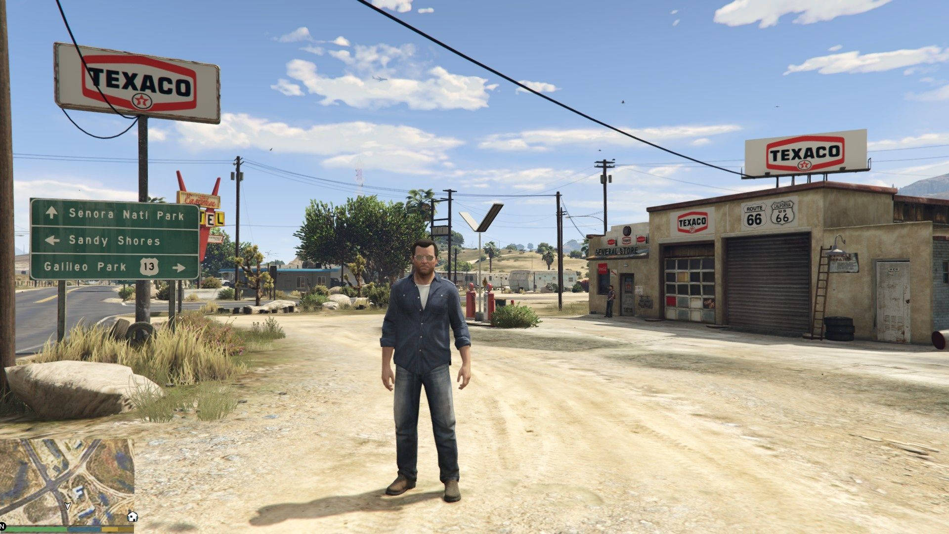 瓦斯 桌布 壁紙 — 一個男人站在塵土飛揚的路邊小鎮，有Texaco加油站和Route 66標誌，天空湛藍明亮。