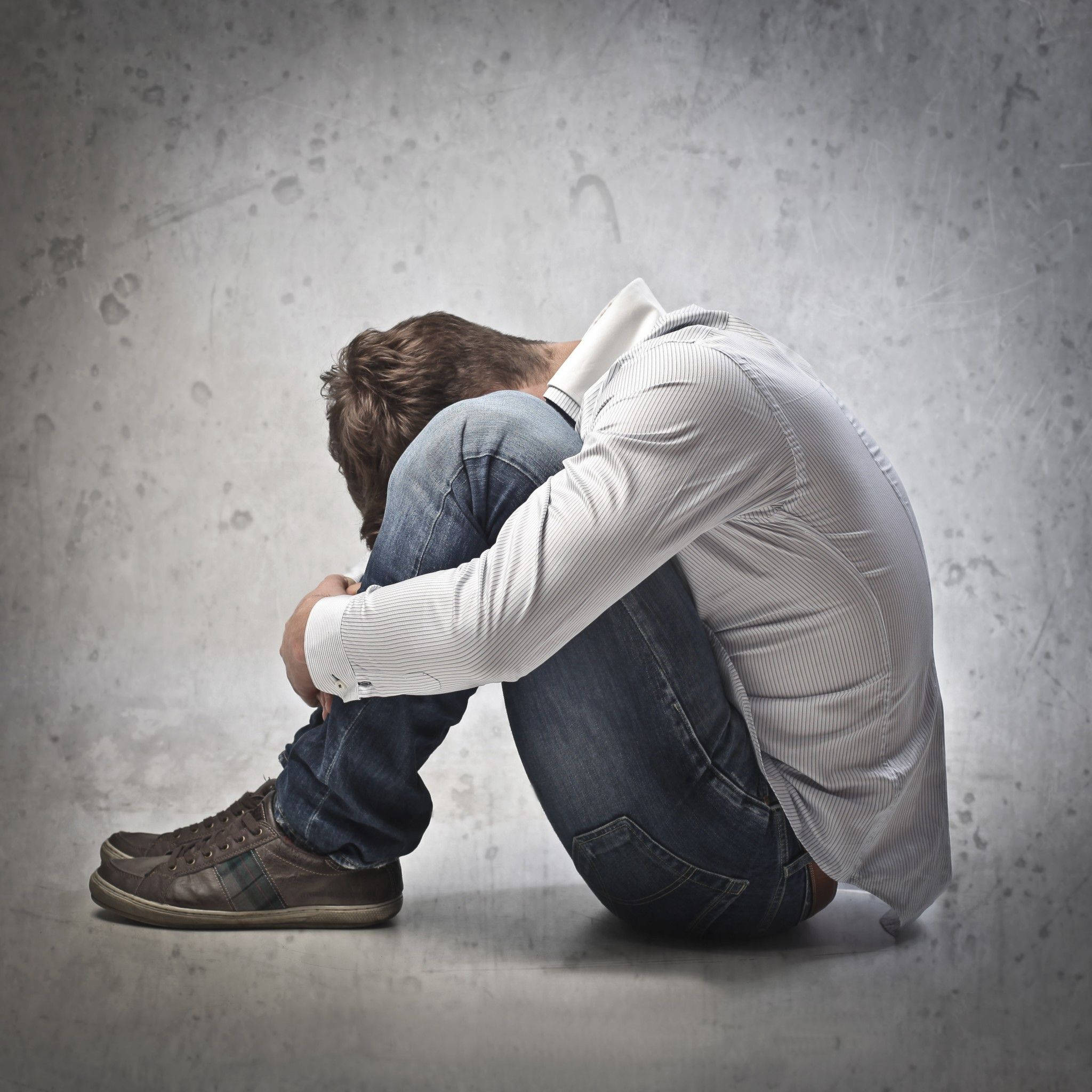 crying sad boy 桌布 壁紙 — 一個男人蜷縮在混凝土的地板上，頭低著靠在有紋理的灰色牆上。