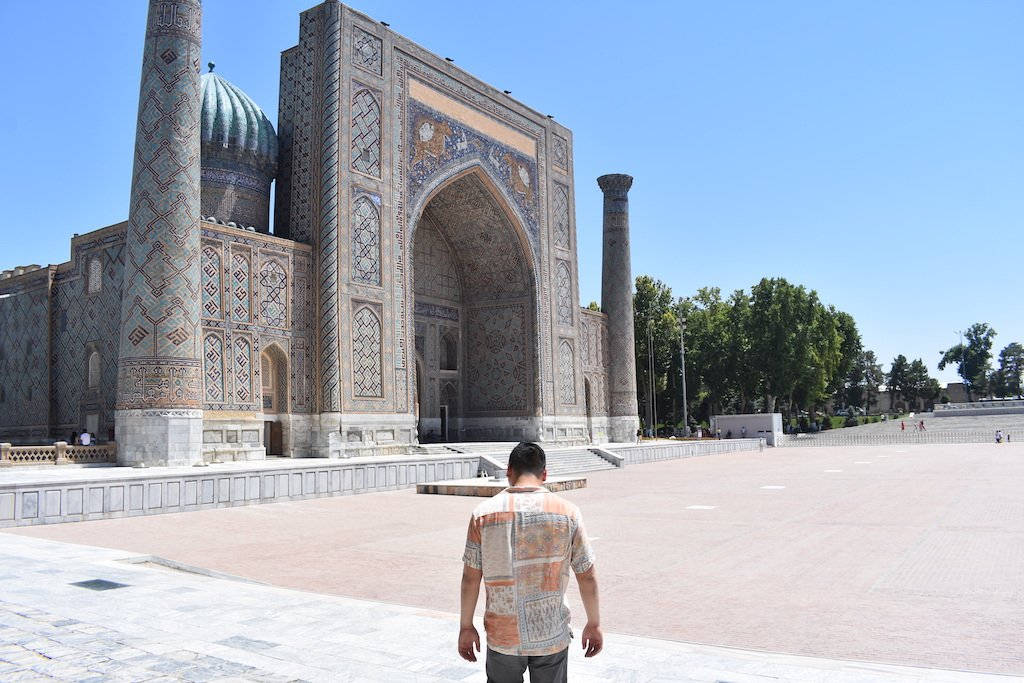 Uzbekistan 桌布 壁紙 — 一個男人走向一座宏偉的歷史清真寺，寺內有精緻的瓷磚工藝，天空清澈湛藍。