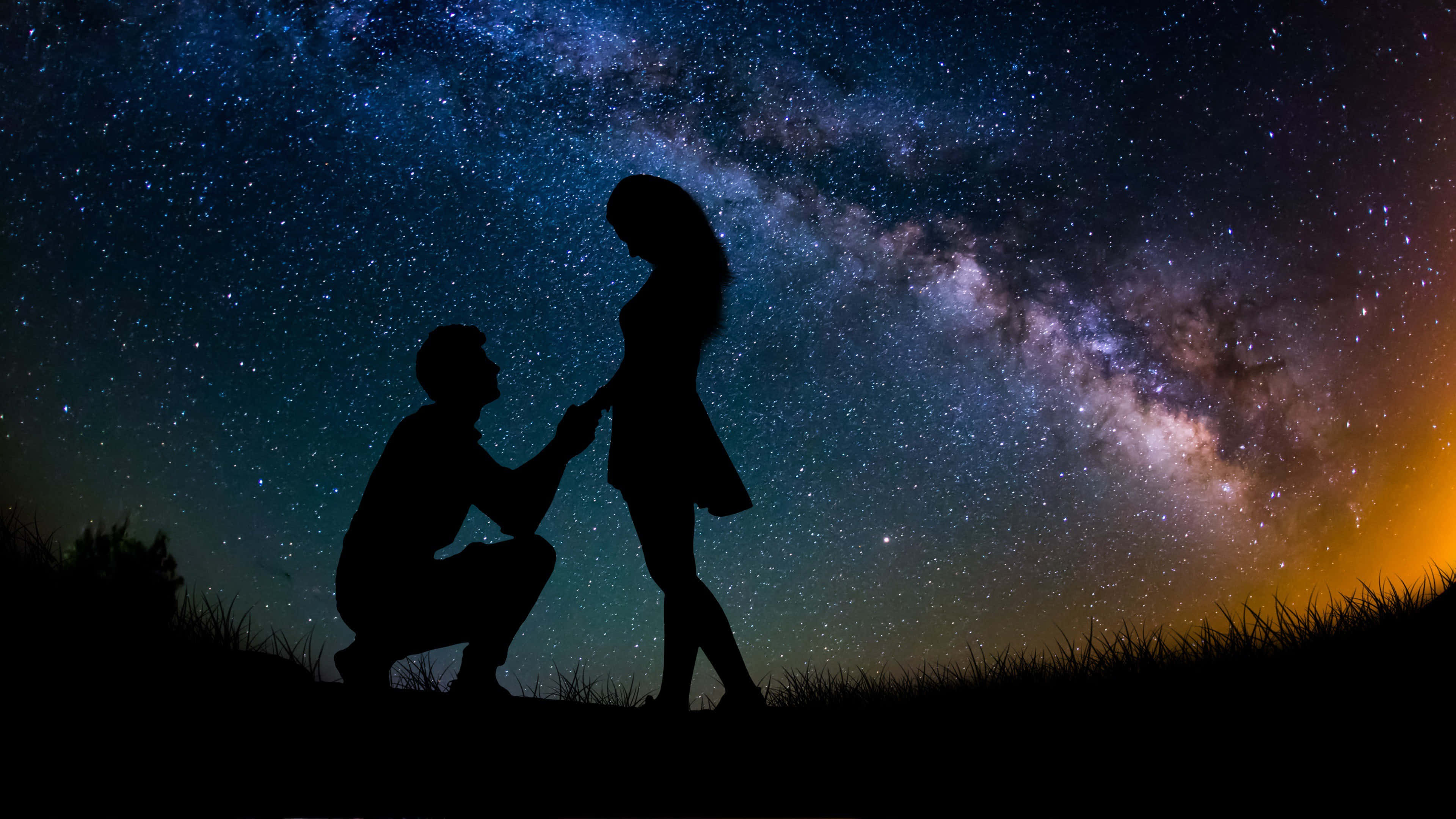 4K Love 桌布 壁紙 — 一個男人跪下來向女人求婚的剪影，背景是壯麗的星空，銀河在他們頭頂彎曲。