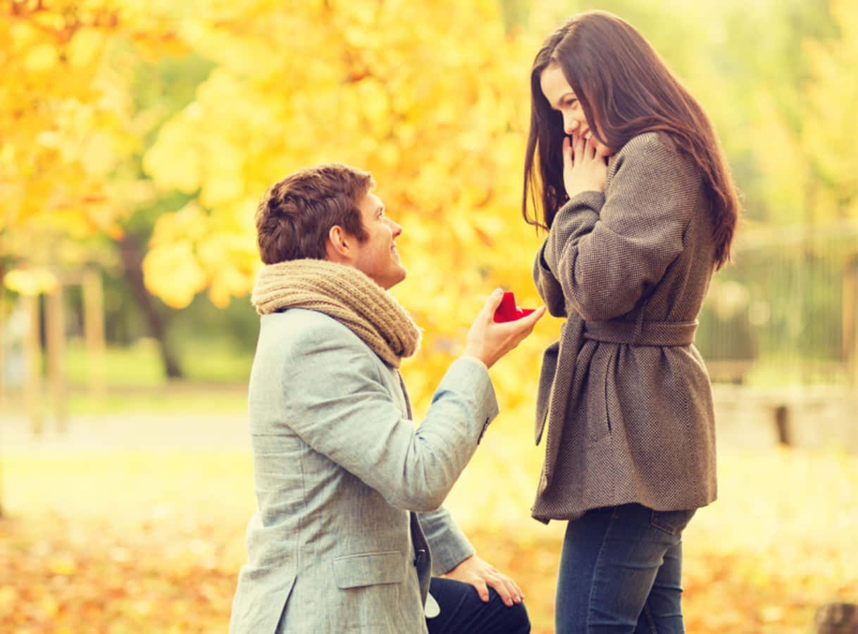 Proposal 桌布 壁紙 — 一個男人跪在金色的秋季公園裡，向一位拿著紅色戒指盒的高興女人求婚。