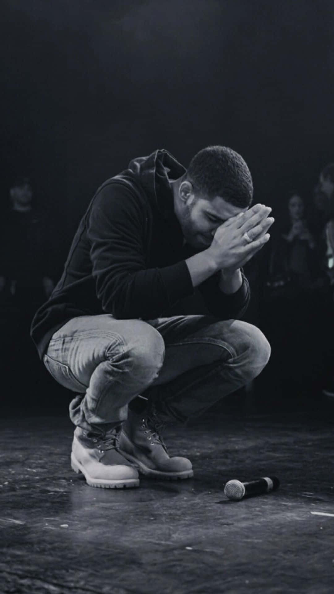 Praying 桌布 壁紙 — 一個男人跪在黑暗的舞台上，雙手掩面，附近有一個被遺棄的麥克風。