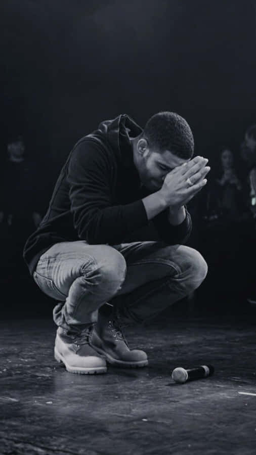 Aesthetic Drake 桌布 壁紙 — 一個男人跪在黑暗的舞台上，雙手掩面，附近有一個被遺棄的麥克風。