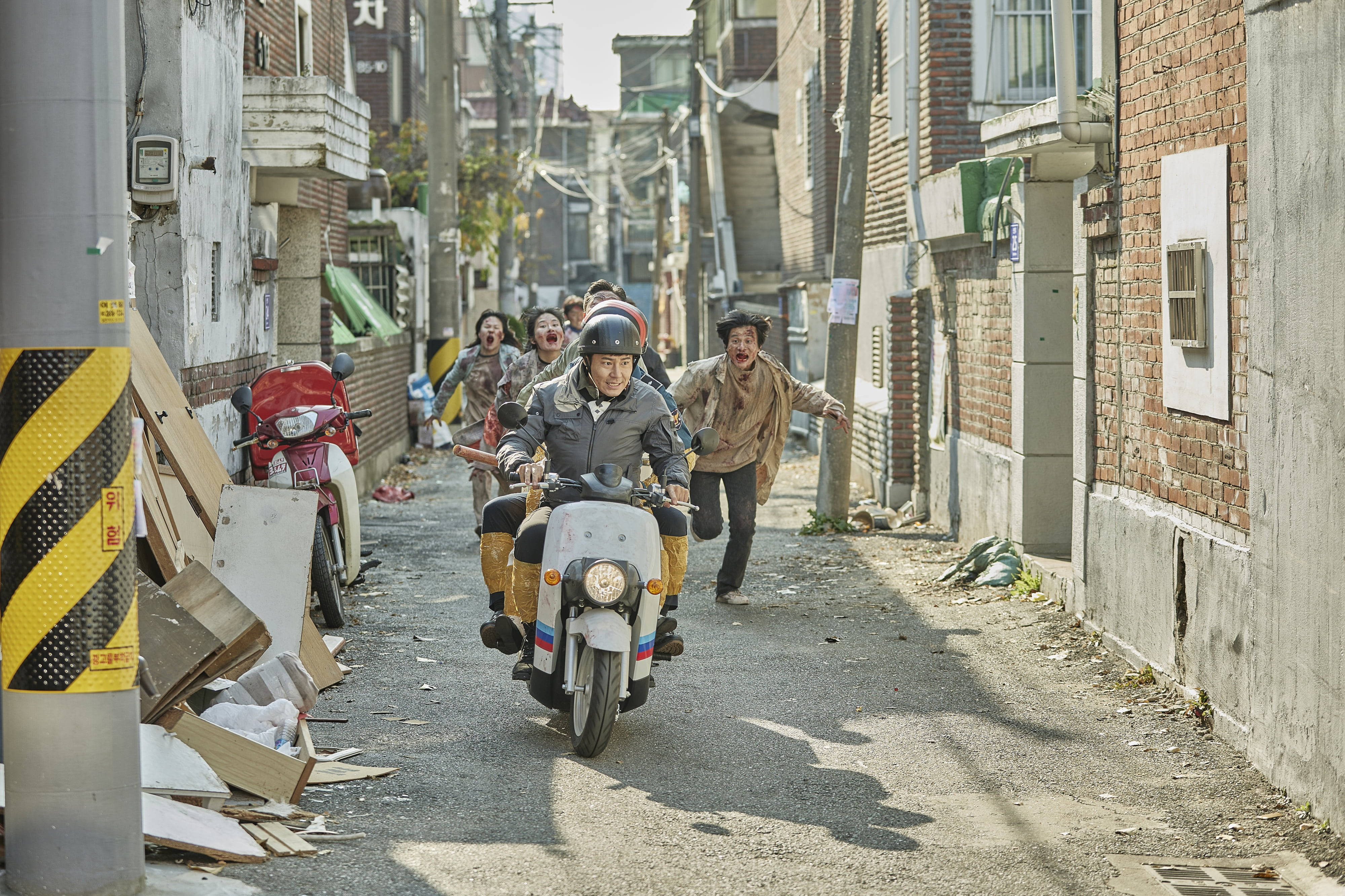 殭屍動圖 桌布 壁紙 — 一個男人騎著滑板車穿過狹窄的小巷，人們帶著瘋狂的表情追趕他。