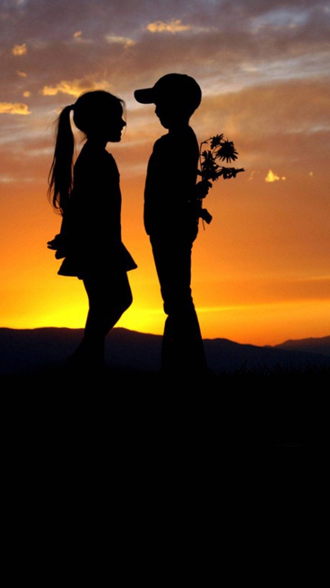 Romantic Love 桌布 壁紙 — 一個男孩和一個女孩的剪影，在充滿活力的橙色日落天空和遠處山巒的襯托下相對而立。