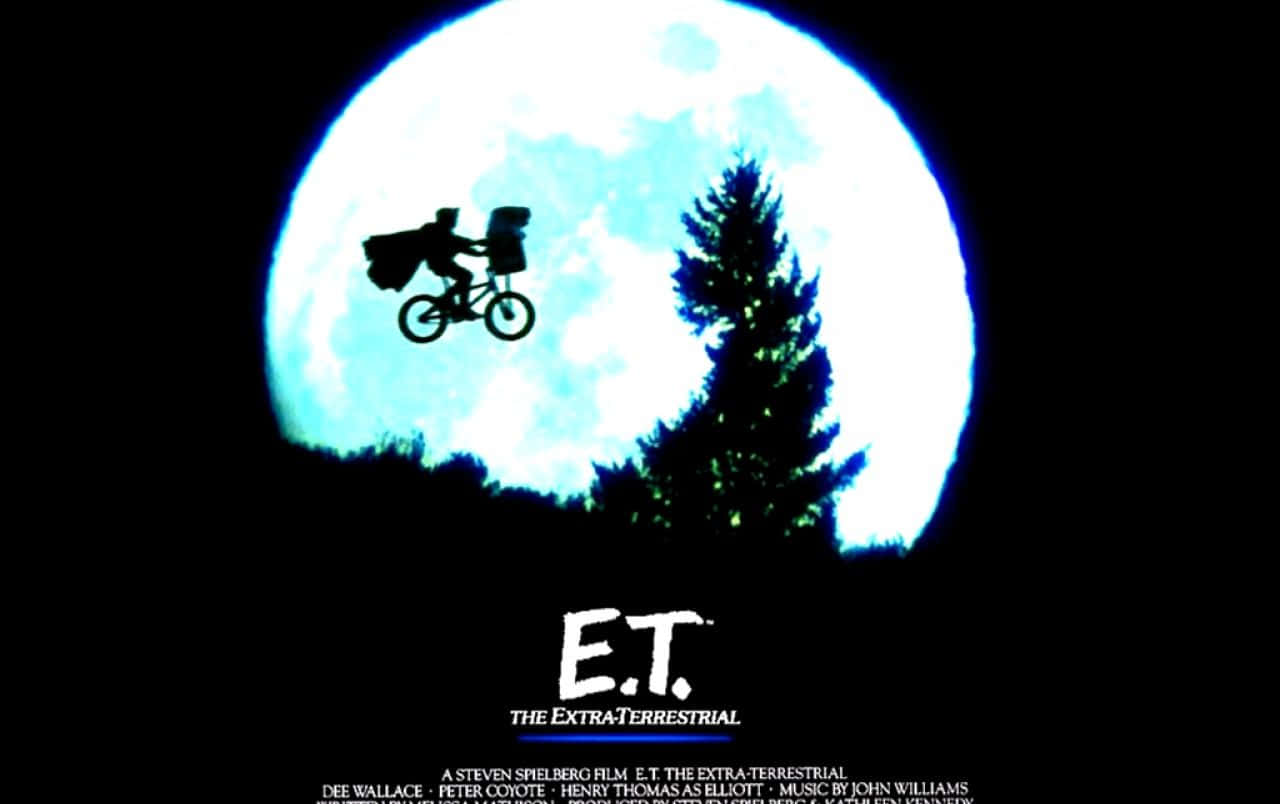 Et 桌布 壁紙 — 一個男孩和外星人騎著腳踏車，背景是一個巨大的發光月亮，旁邊有一棵松樹的剪影。