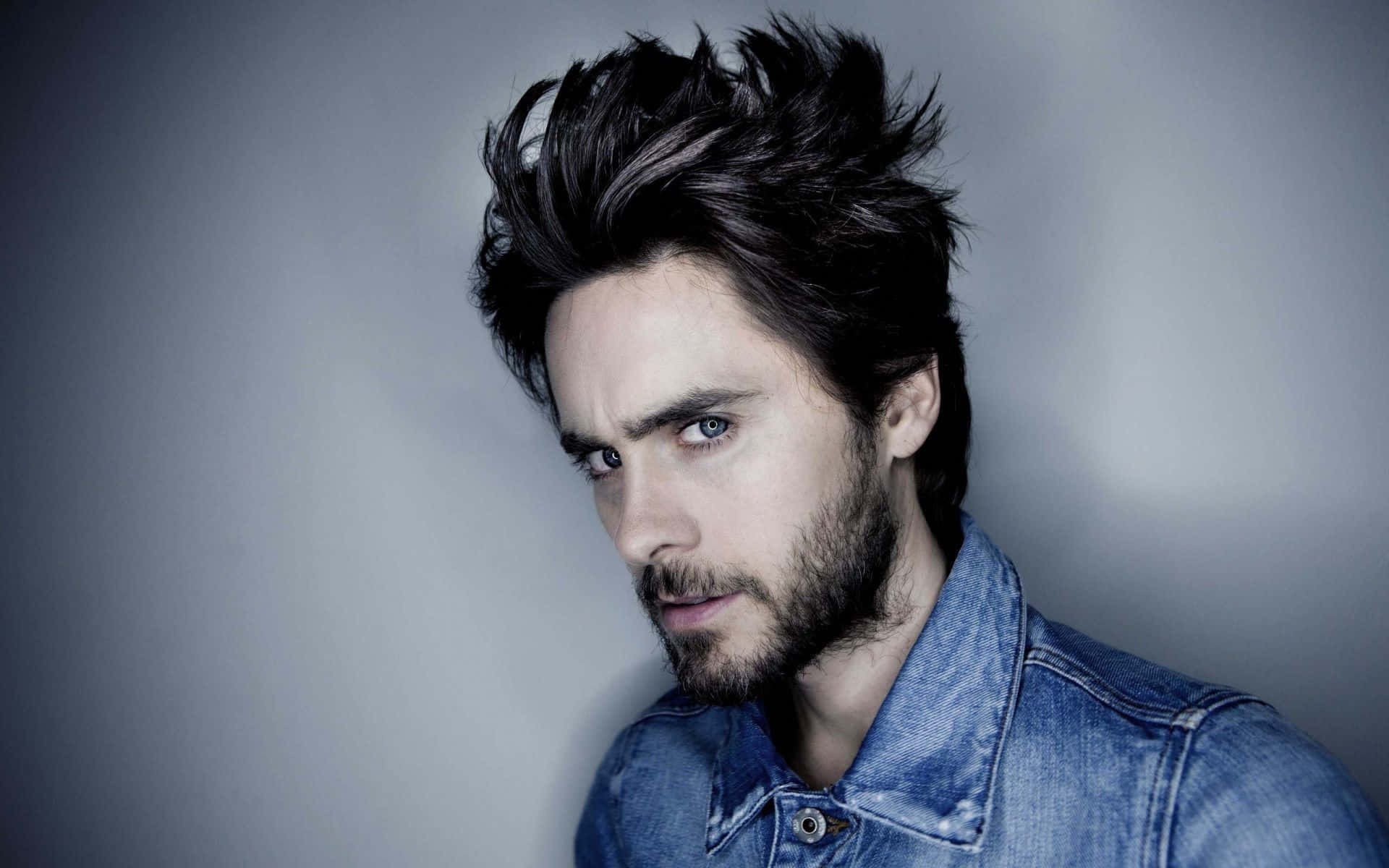 jared leto 桌布 壁紙 — 一個留著刺蝟般深色頭髮和鬍鬚的男人，穿著牛仔襯衫，在灰色背景下凝視著鏡頭。