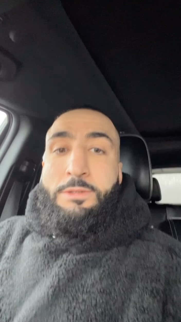 Celebrity 桌布 壁紙 — 一個留著大鬍子的男人穿著灰色絨毛連帽衫，坐在黑色內裝的車內。