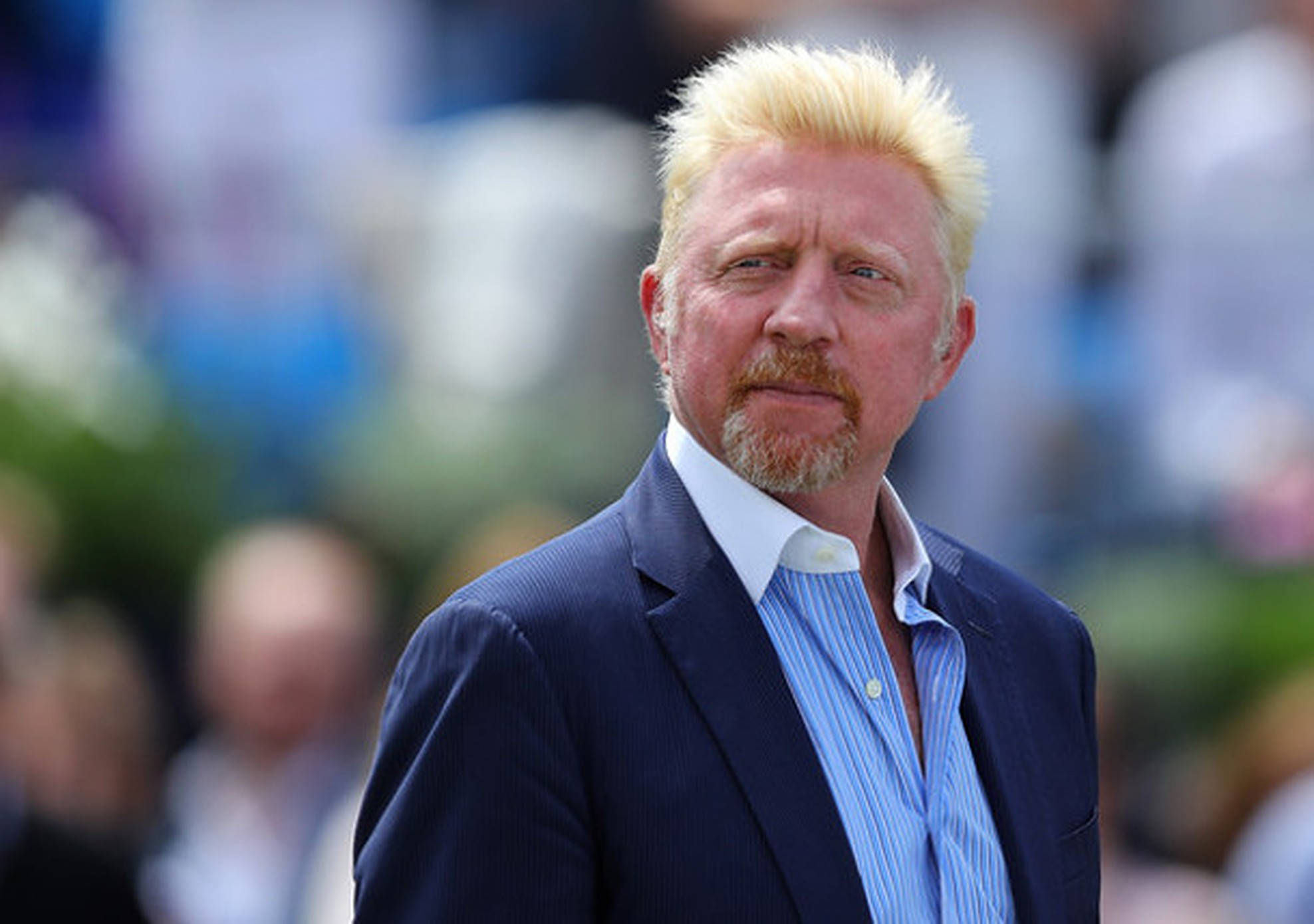 Boris Becker 桌布 壁紙 — 一個留著尖刺金髮和山羊鬍的男人，身穿海軍藍西裝，內搭藍色條紋襯衫，背景是模糊的人群。