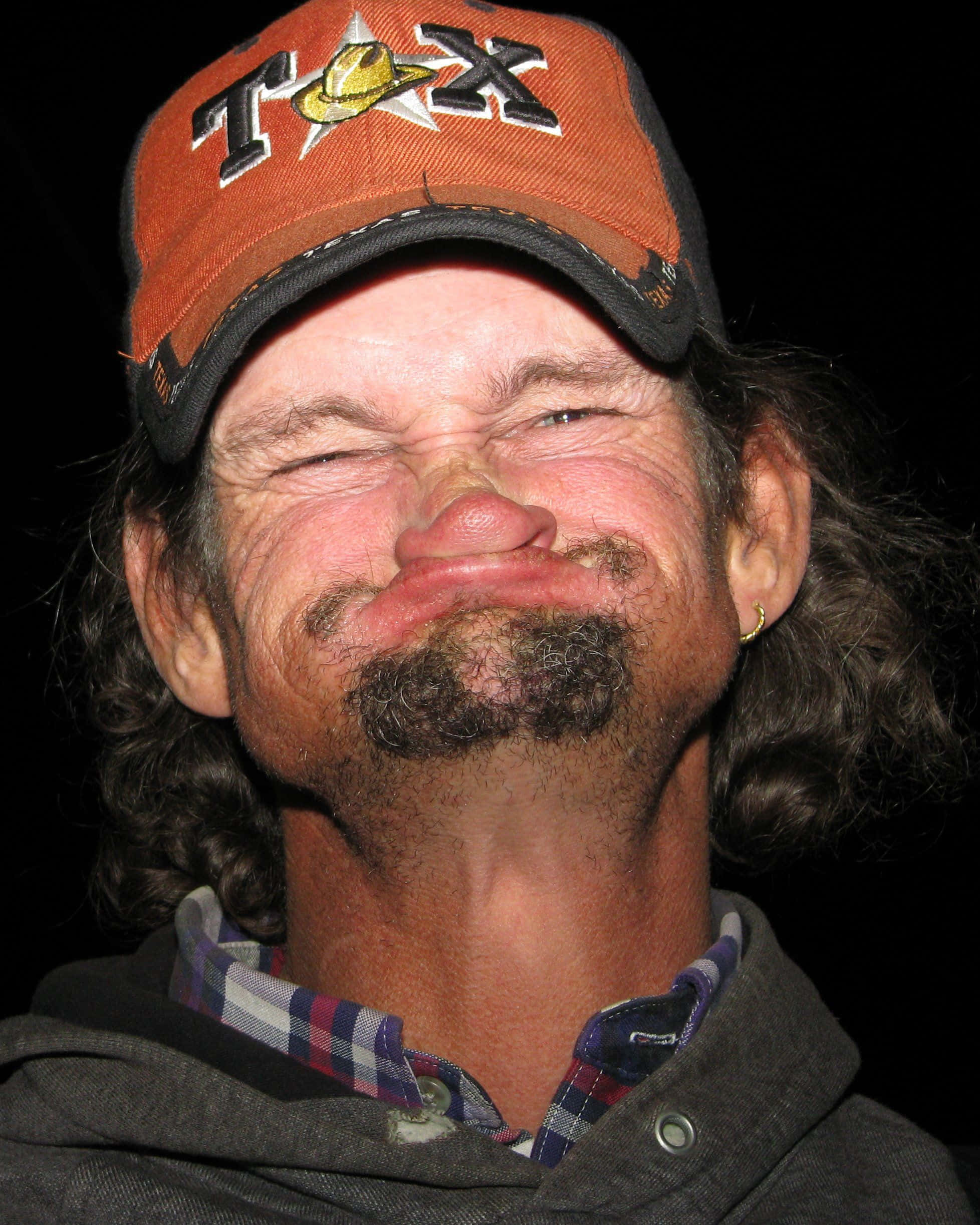 Funny Face 桌布 壁紙 — 一個留著山羊鬍和長髮的男人，戴著橙色德州帽，在黑色背景前開懷大笑。