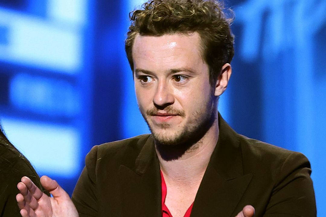 Celebrity 桌布 壁紙 — 一個留著捲髮和鬍鬚的男人在模糊的藍色背景前說話時做手勢。