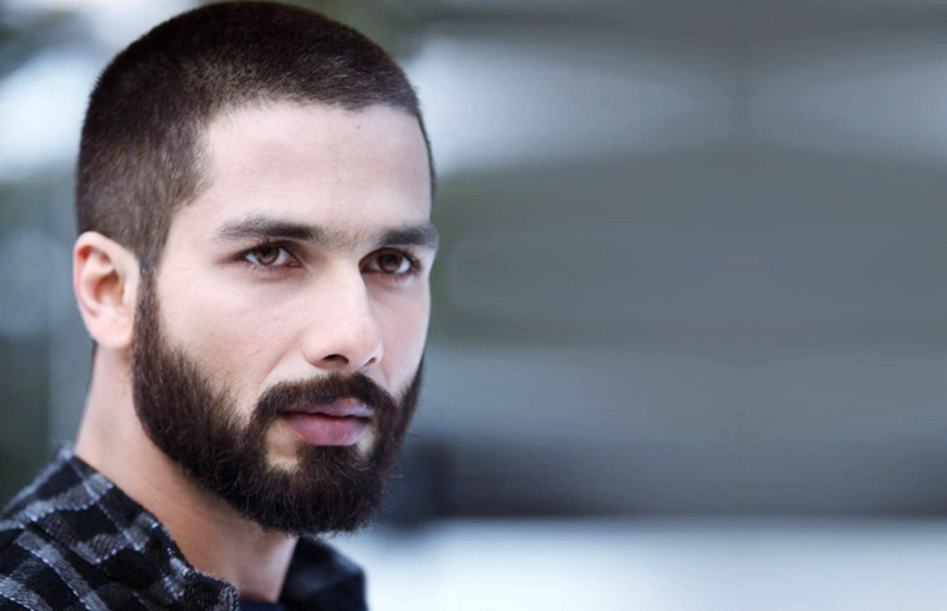 Shahid Kapoor 桌布 壁紙 — 一個留著深色鬍鬚和短髮的男人，在模糊的城市背景下專注地看著鏡頭的近距離肖像。