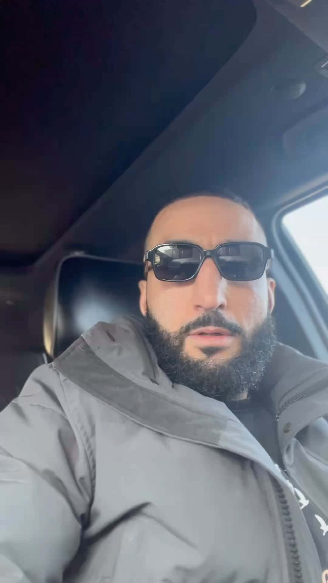 Celebrity 桌布 壁紙 — 一個留著濃密鬍鬚、戴著太陽眼鏡的男人坐在車內，穿著灰色外套，看著相機。