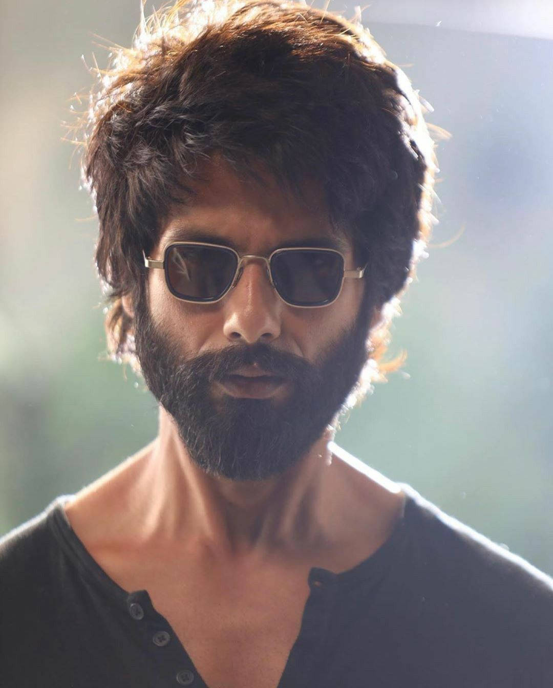 Shahid Kapoor 桌布 壁紙 — 一個留著濃密鬍鬚、戴著太陽眼鏡的男人，在柔和模糊的背景和溫暖的逆光中凝視著。