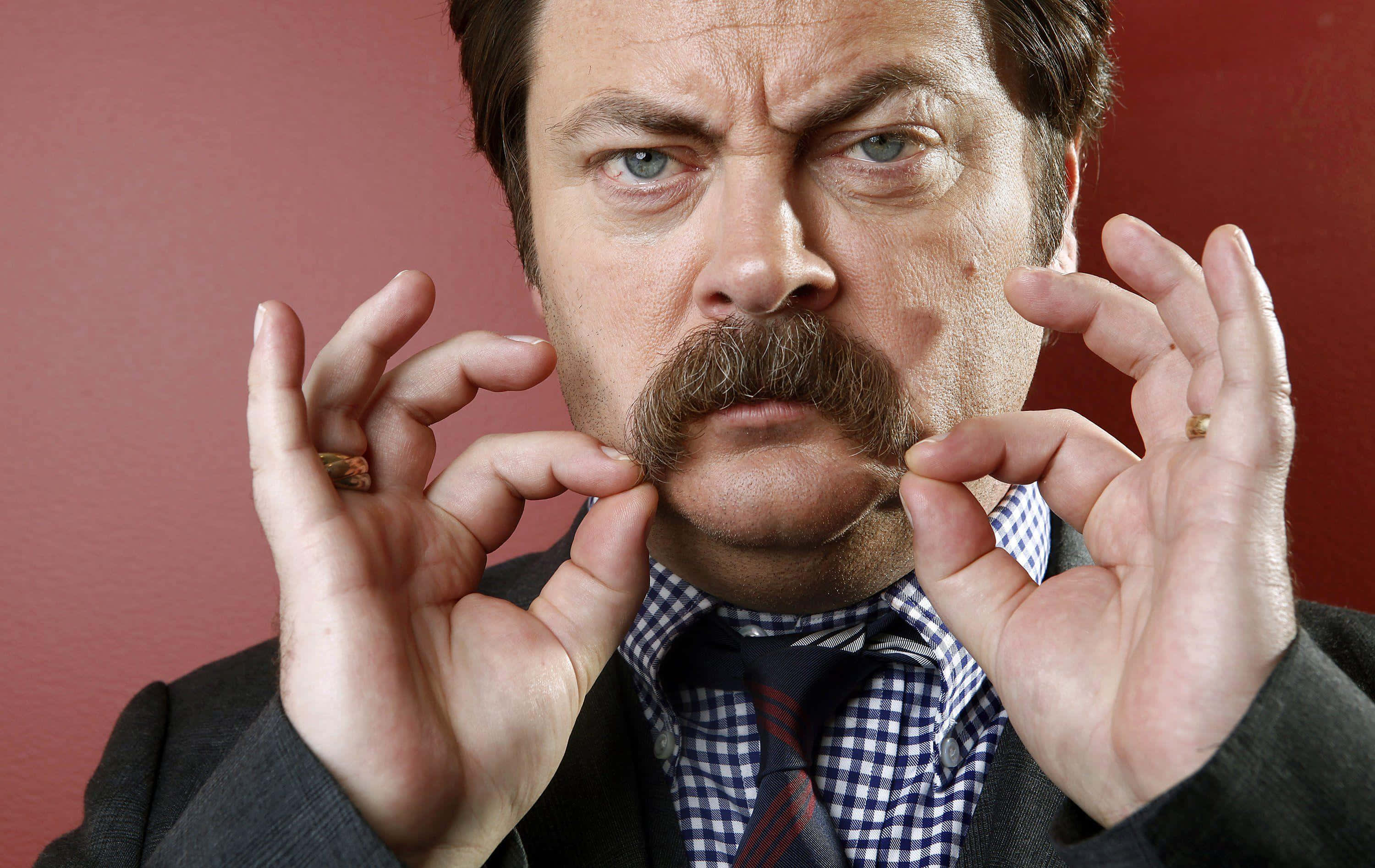 nick offerman 桌布 壁紙 — 一個留著濃密鬍鬚、眼神銳利的男人，在純紅色背景前用手指捏著他的鬍鬚。