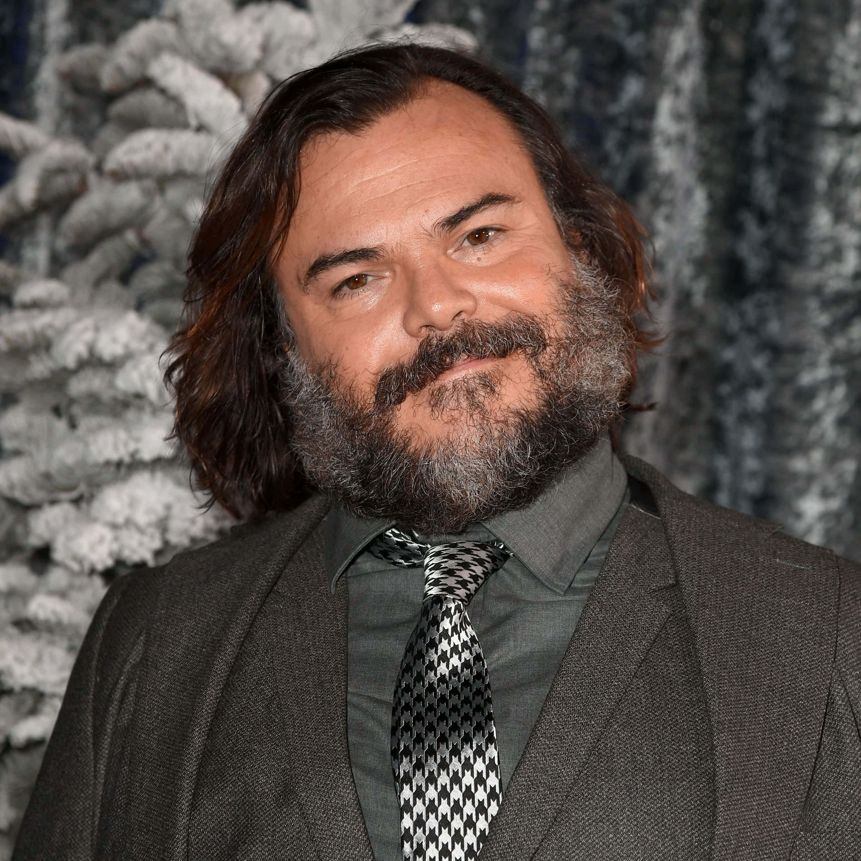 jack black 桌布 壁紙 — 一個留著濃密鬍鬚和長髮的男人，穿著灰色西裝和圖案領帶，背景是白雪覆蓋的松樹。