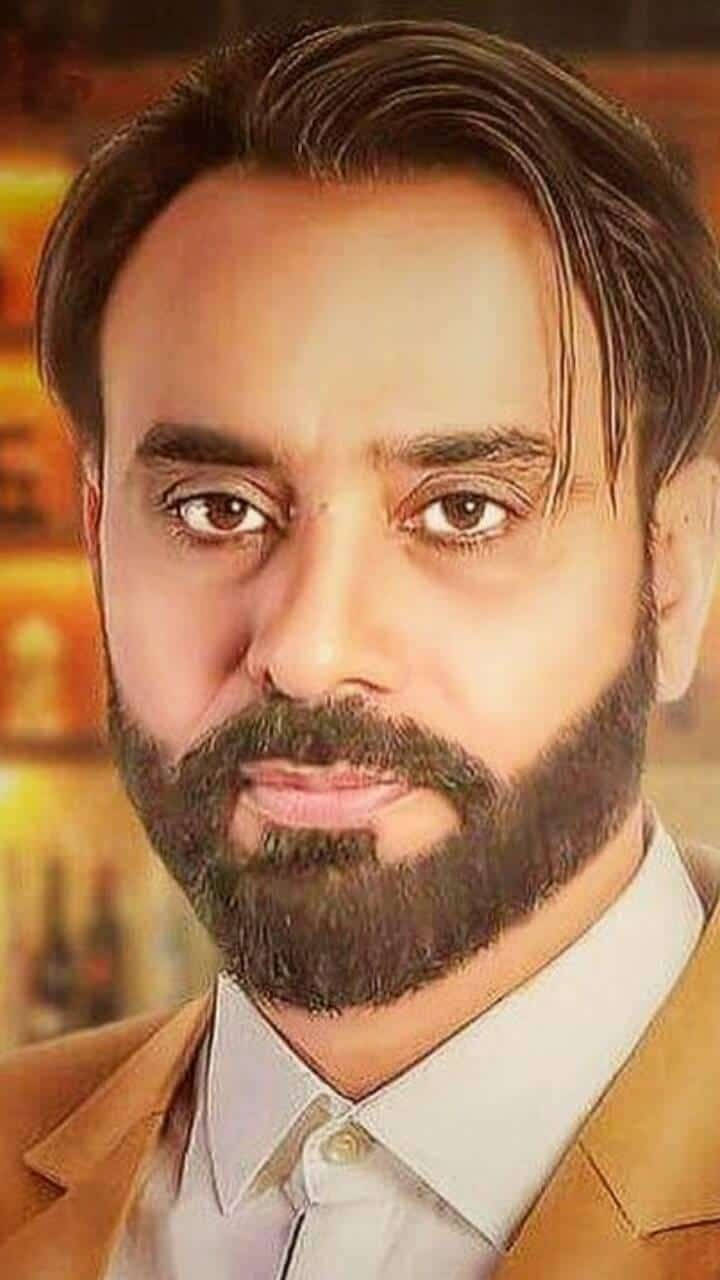 Indian 桌布 壁紙 — 一個留著濃密鬍鬚的男人特寫肖像，身穿米色西裝外套內搭白襯衫，背景是溫暖燈光的模糊效果。