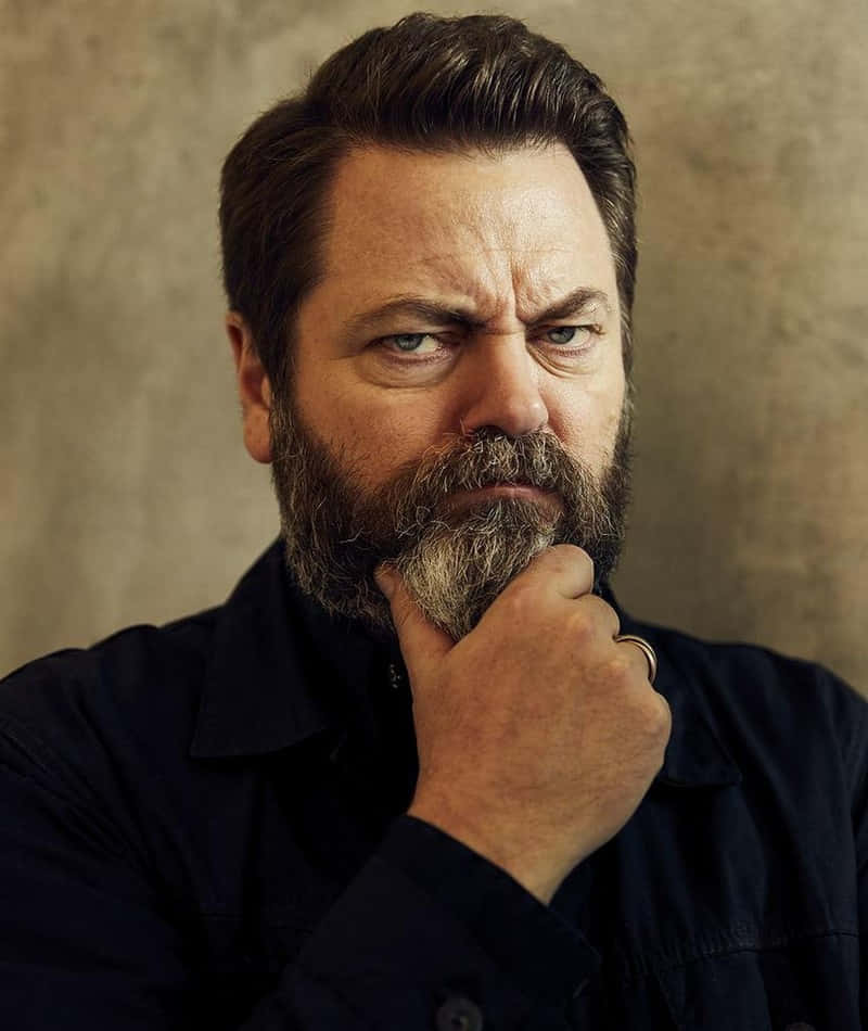 nick offerman 桌布 壁紙 — 一個留著灰白鬍鬚、眼神銳利的男人，將下巴擱在手上，靠著紋理米色牆壁。