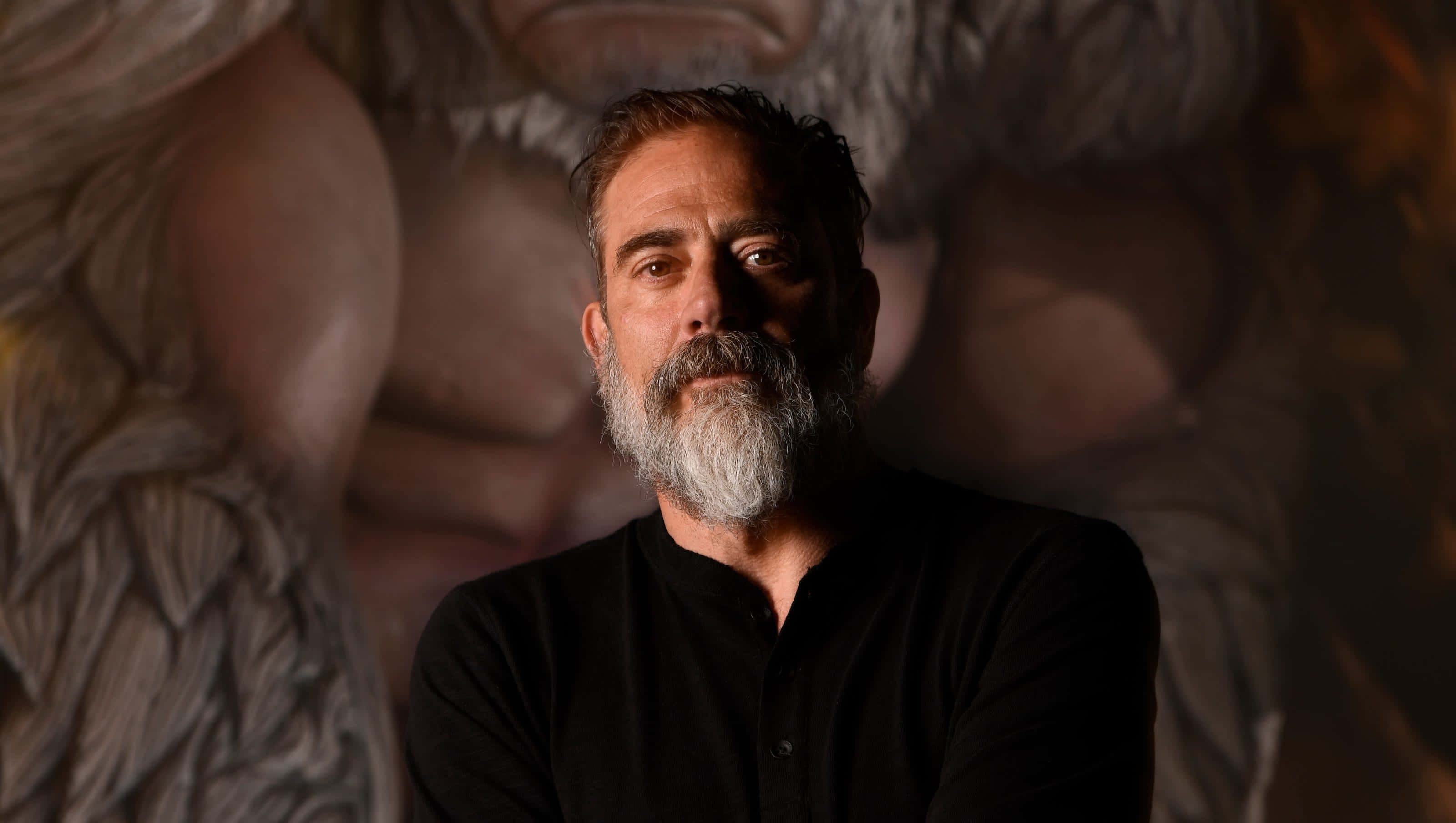 jeffrey dean morgan 桌布 壁紙 — 一個留著灰色鬍鬚的男人在燈光昏暗的房間裡向前凝視，身後有一幅巨大的神話壁畫。