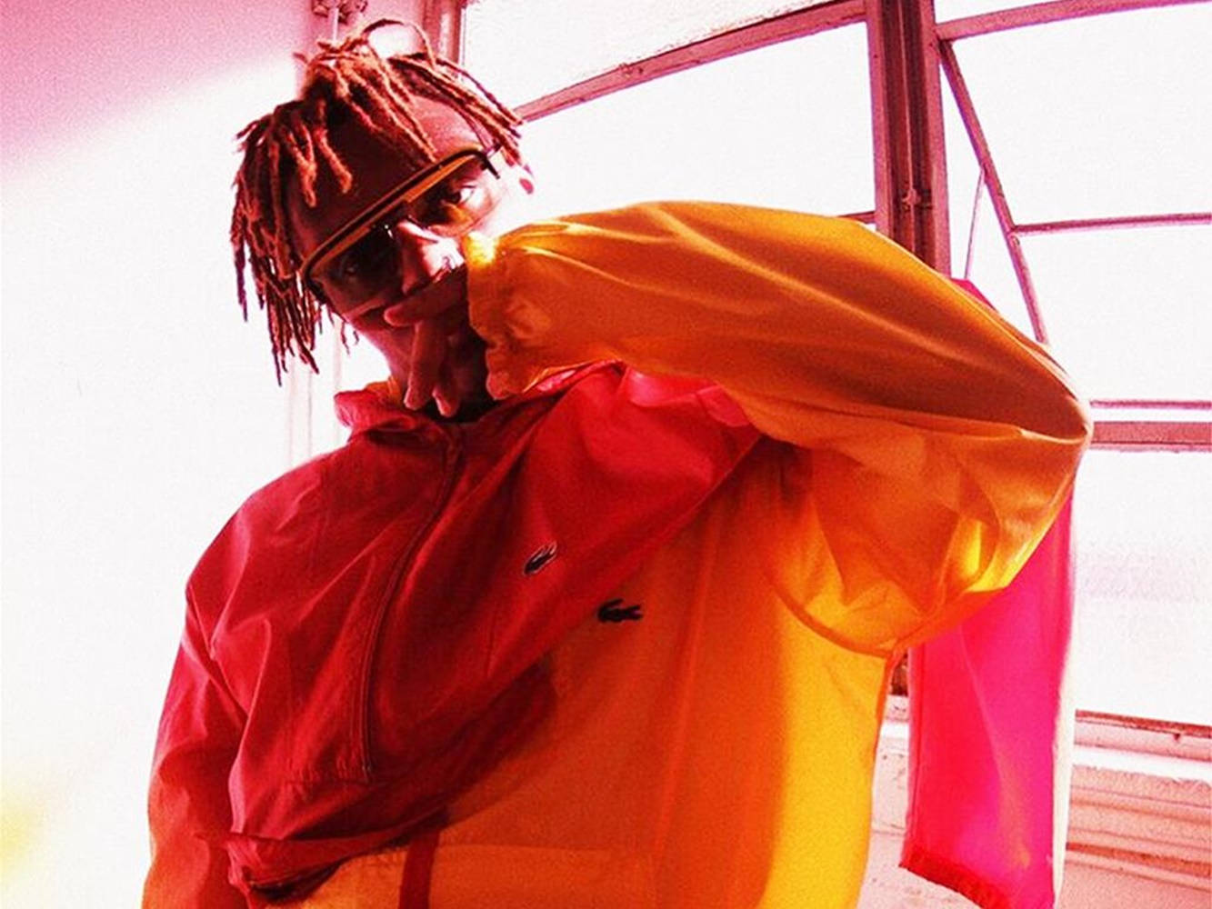 留著紅色辮子、戴著太陽眼鏡的人，在窗邊穿著漸層外套。 — Juice Wrld 壁紙