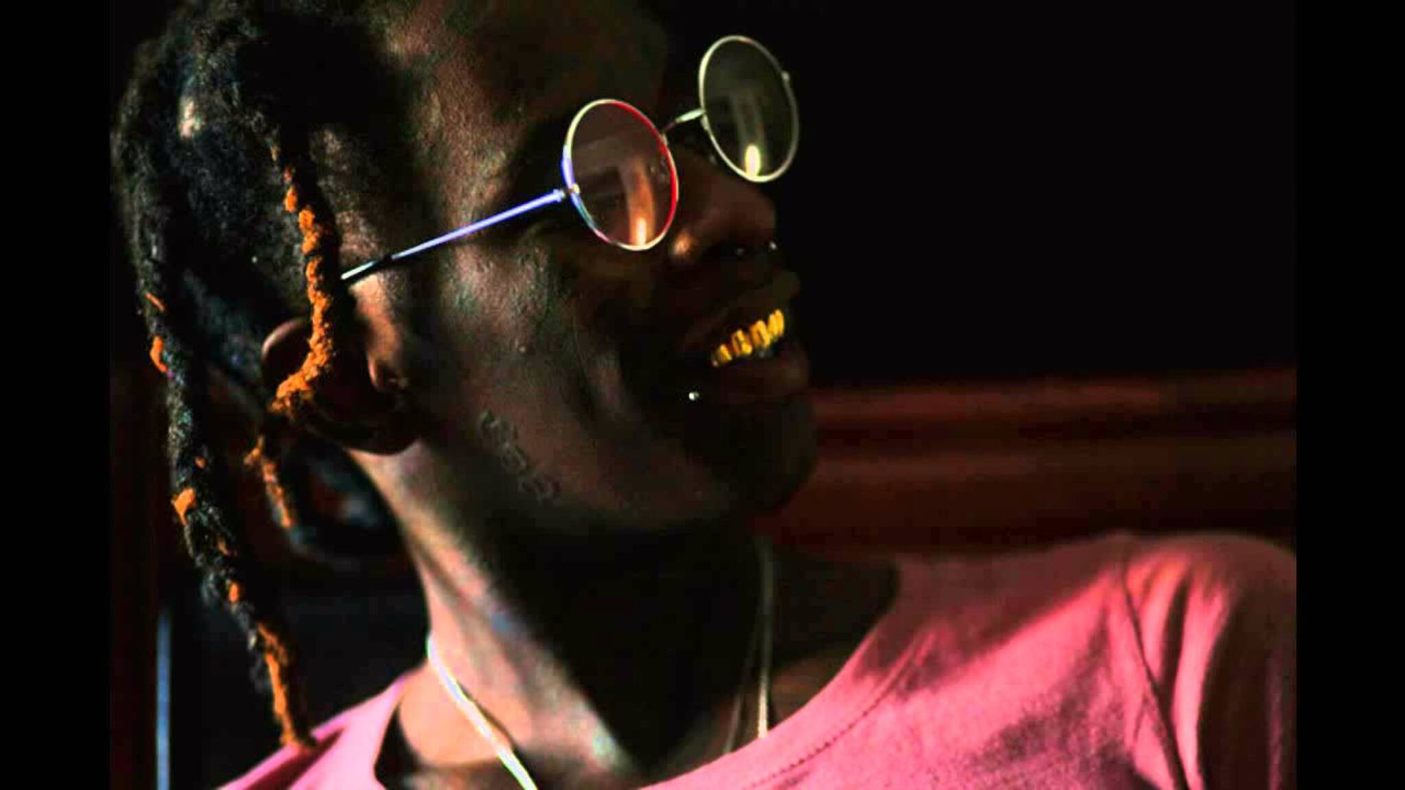 Thug 桌布 壁紙 — 一個留著辮子、戴圓框眼鏡的人，在溫暖燈光下穿著粉紅色襯衫，開懷大笑。