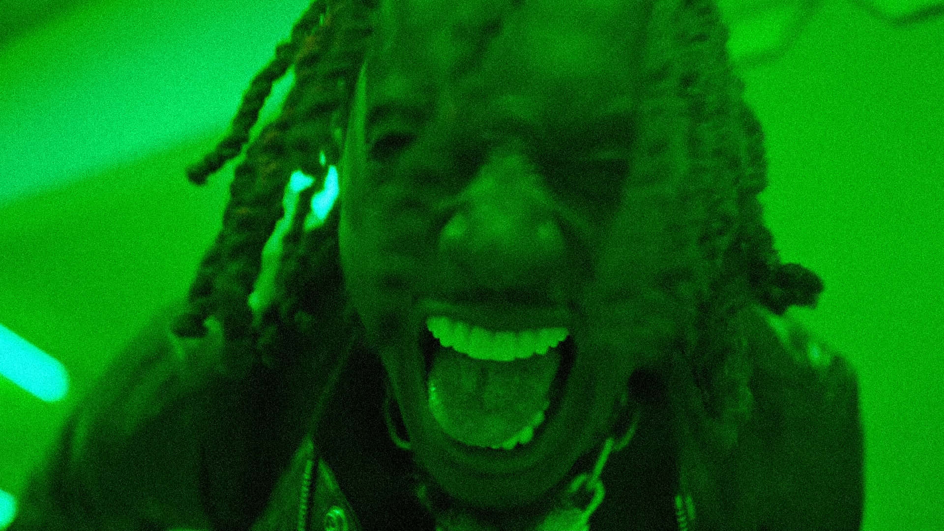 Rappers 桌布 壁紙 — 一個留著辮子的人在強烈的綠色燈光下張開嘴尖叫。