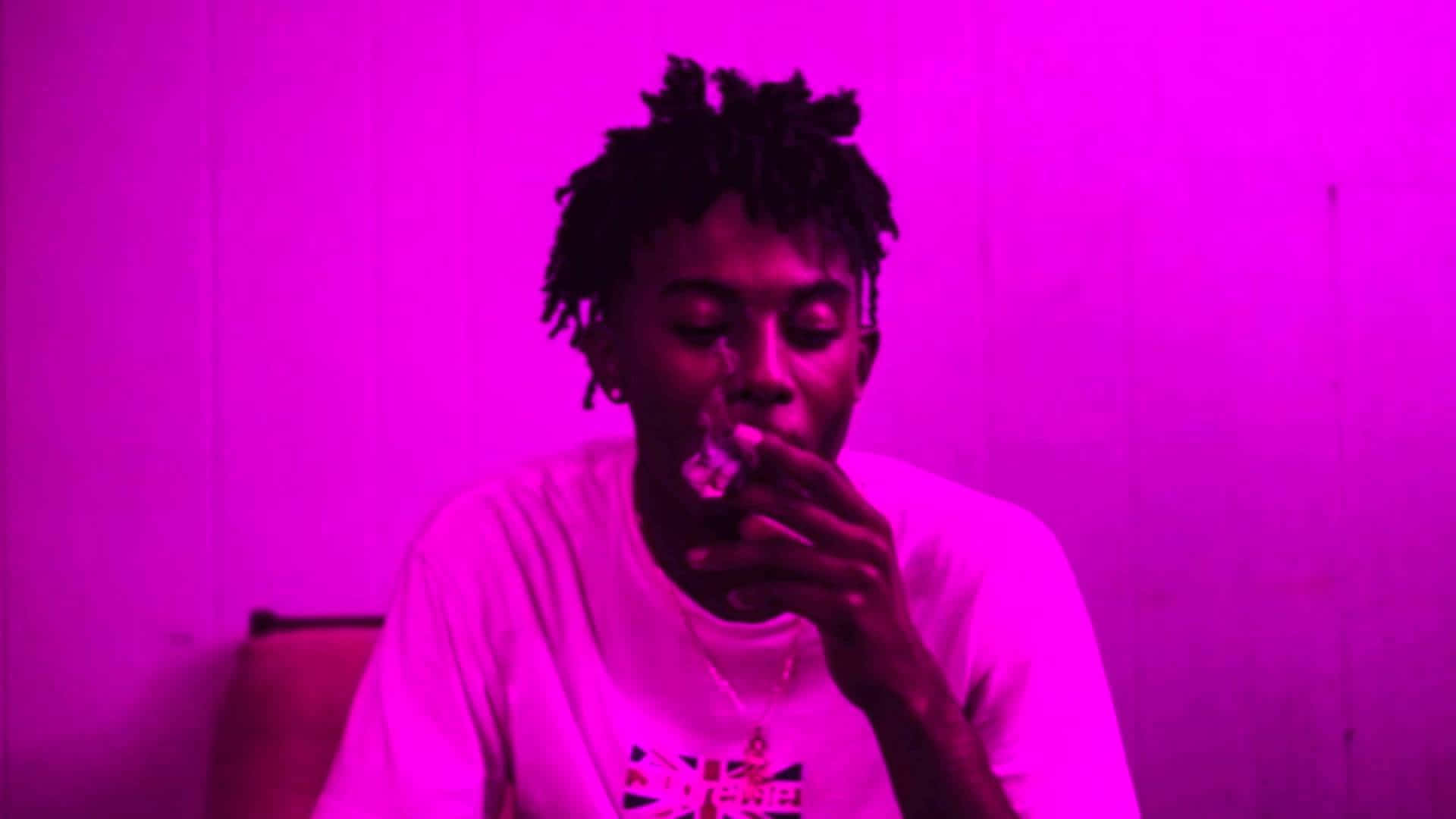 Playboi Carti HD 桌布 壁紙 — 一個留著辮子的人在昏暗的房間裡，在強烈的洋紅色燈光下吸電子煙。