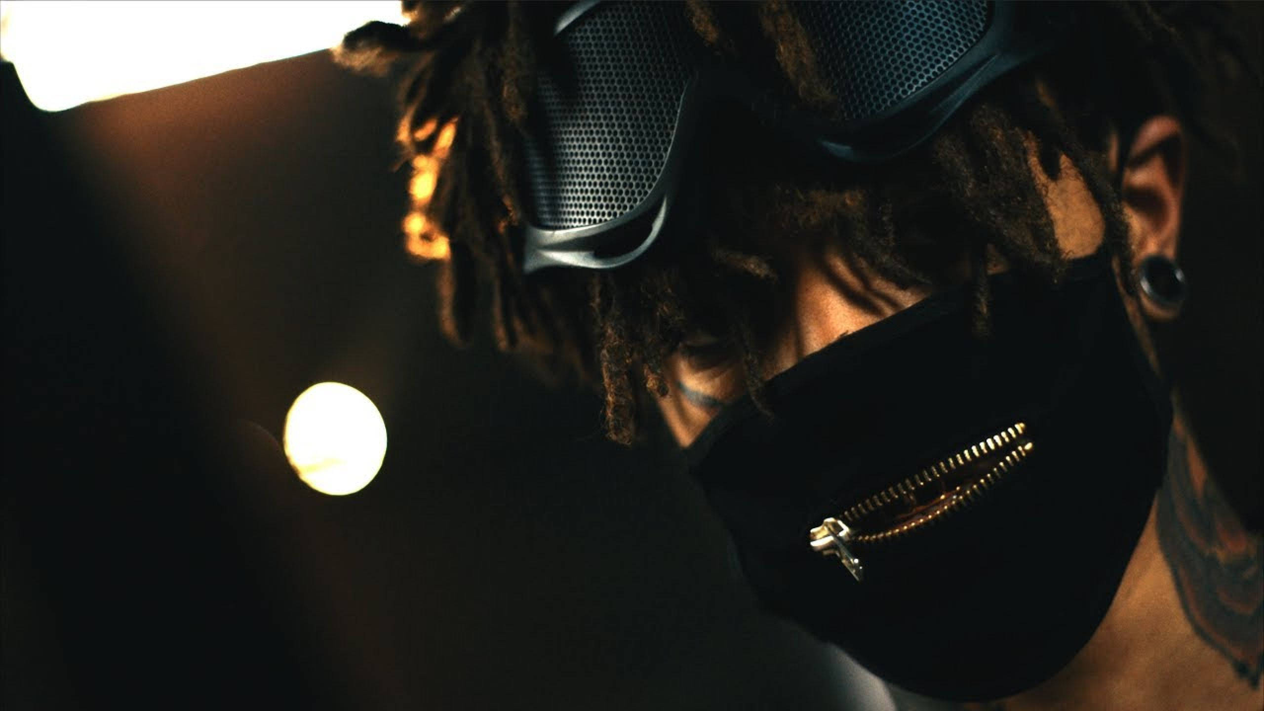 scarlxrd 桌布 壁紙 — 一個留著辮子的人的特寫，戴著黑色拉鍊面罩和網眼護目鏡，在溫暖的電影燈光下。