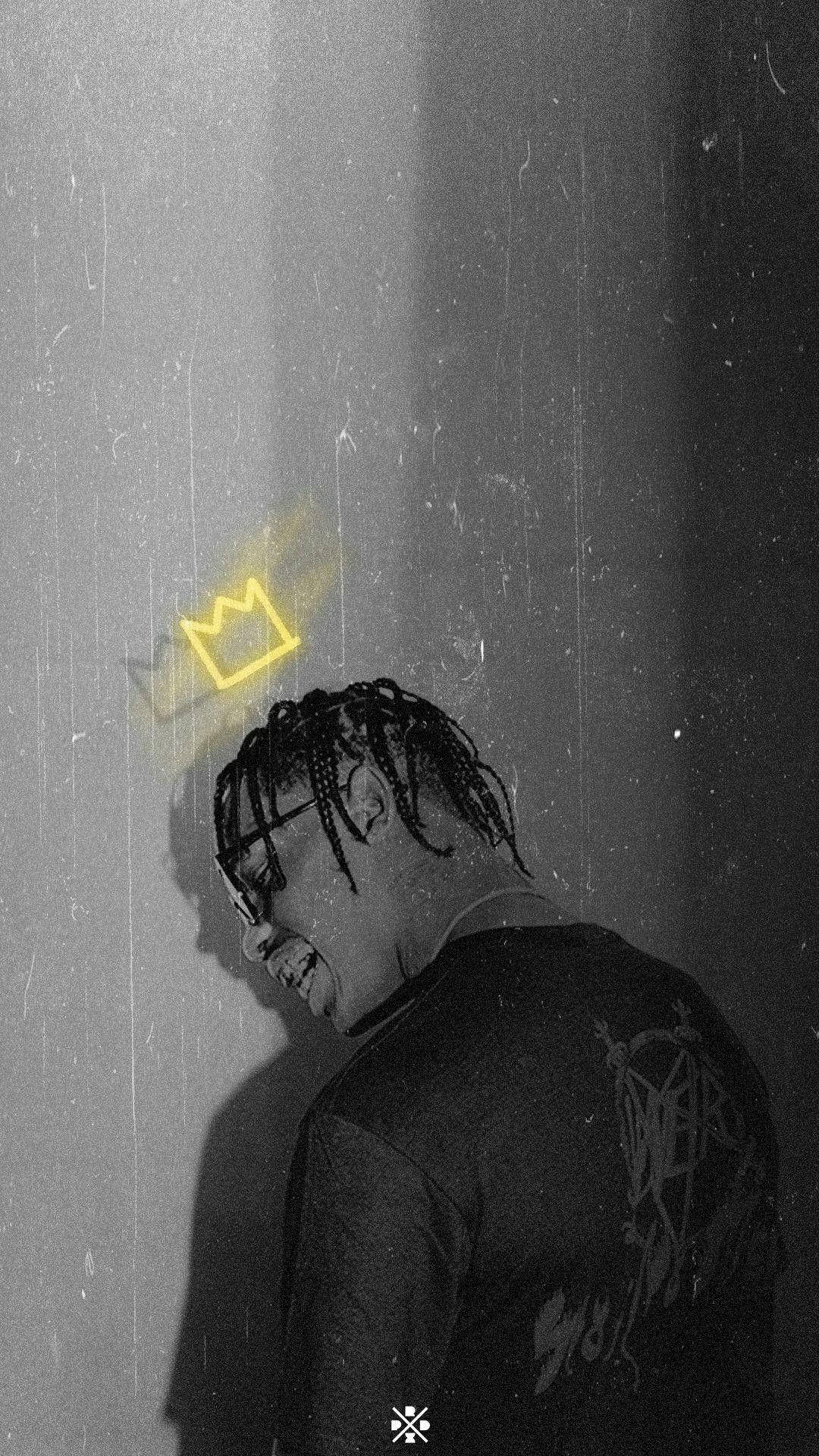 Travis Scott Astroworld 桌布 壁紙 — 一個留著辮子頭、戴眼鏡的人靠著紋理牆壁，一個發光的黃色皇冠懸浮在他們頭頂上方。