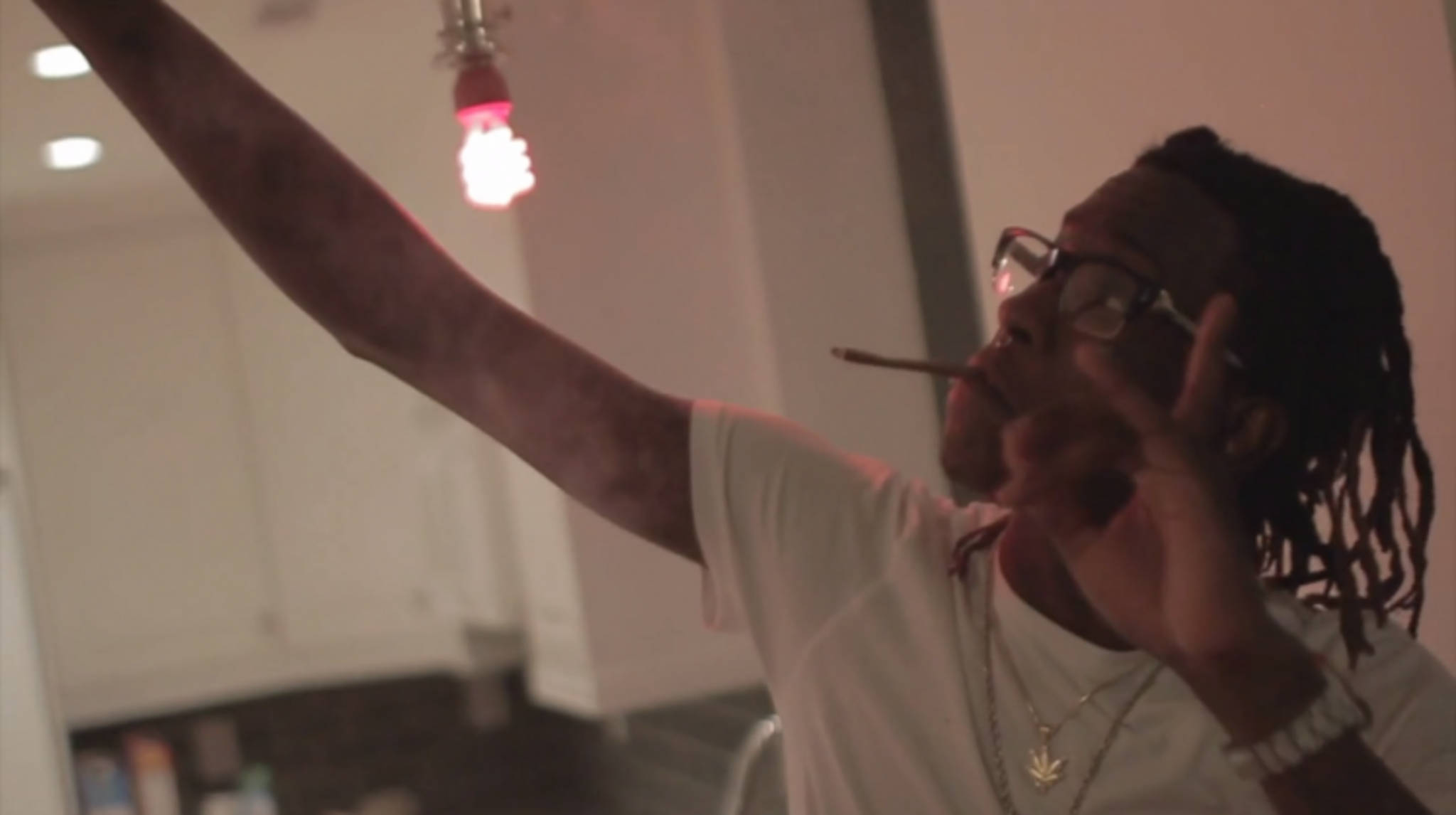 Thug 桌布 壁紙 — 一個留著辮子頭、戴眼鏡的男人在廚房的紅色燈泡下拿著香煙，比出和平手勢。