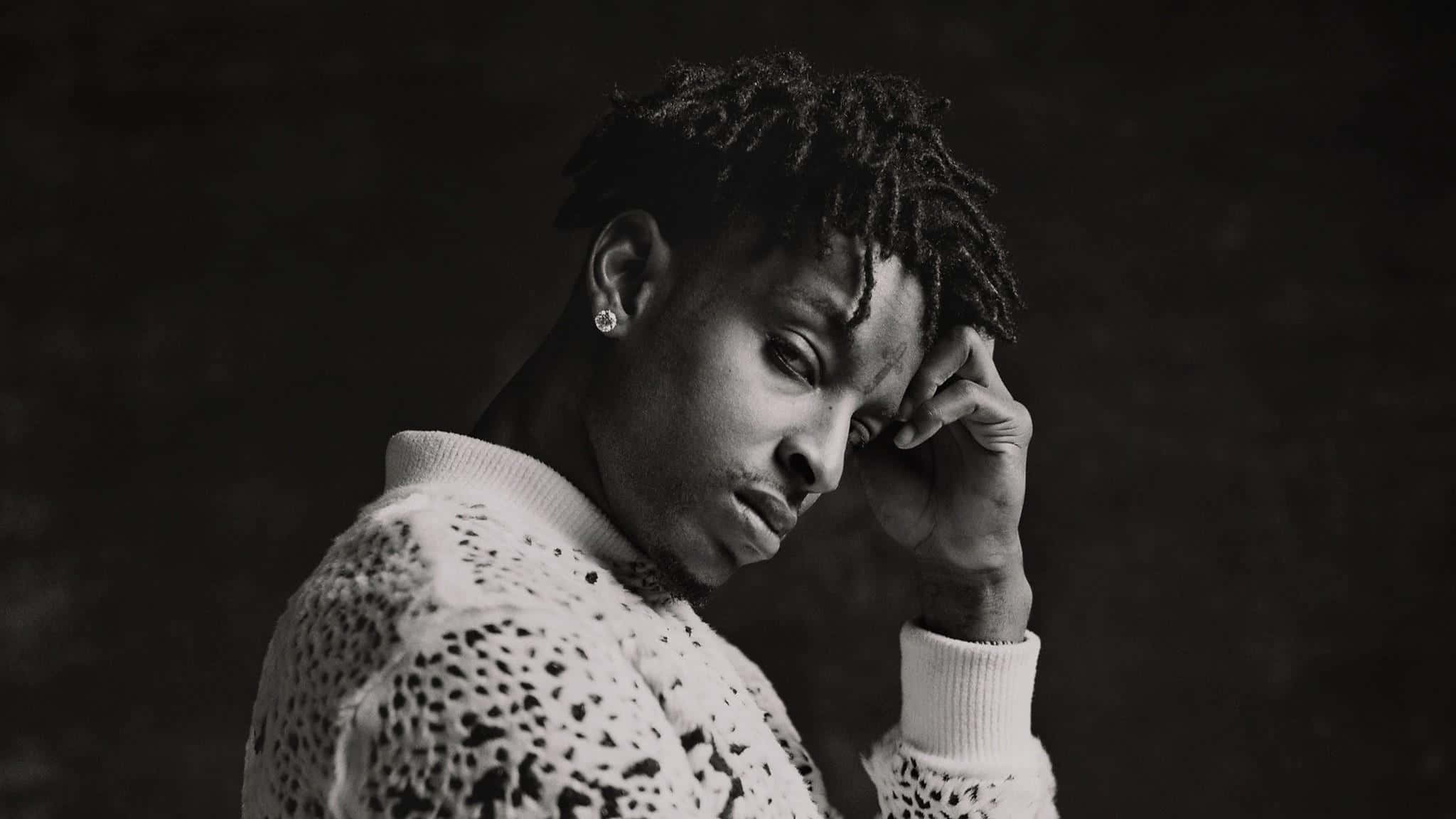21 Savage 桌布 壁紙 — 一個留著辮子頭的男人以沉思姿態觸碰額頭的黑白肖像。