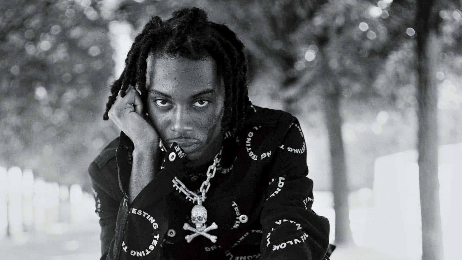 Playboi Carti 桌布 壁紙 — 一個留著辮子頭的男人在戶外將頭靠在手上的黑白肖像。
