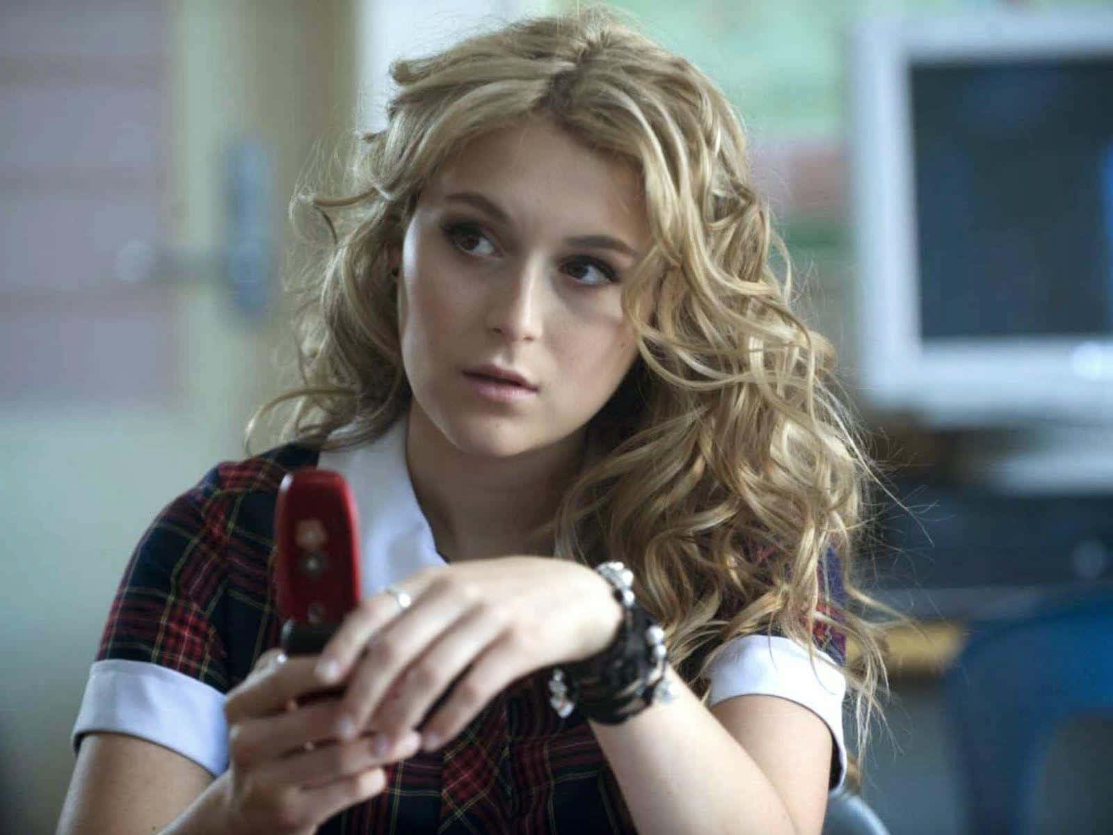 Alexa Penavega 桌布 壁紙 — 一個留著金色捲髮的少女在教室裡拿著一支紅色折疊手機。