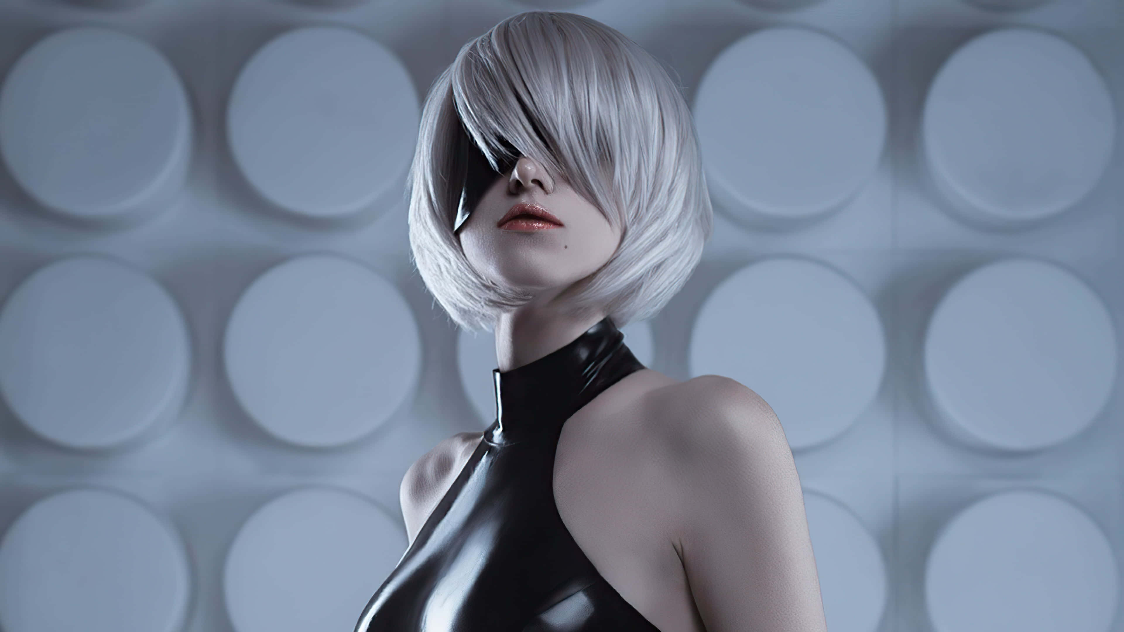 Gaming Cosplay 桌布 壁紙 — 一個留著銀色鮑伯頭、身穿黑色乳膠服裝的人，靠在一面灰色圓形面板的牆上。