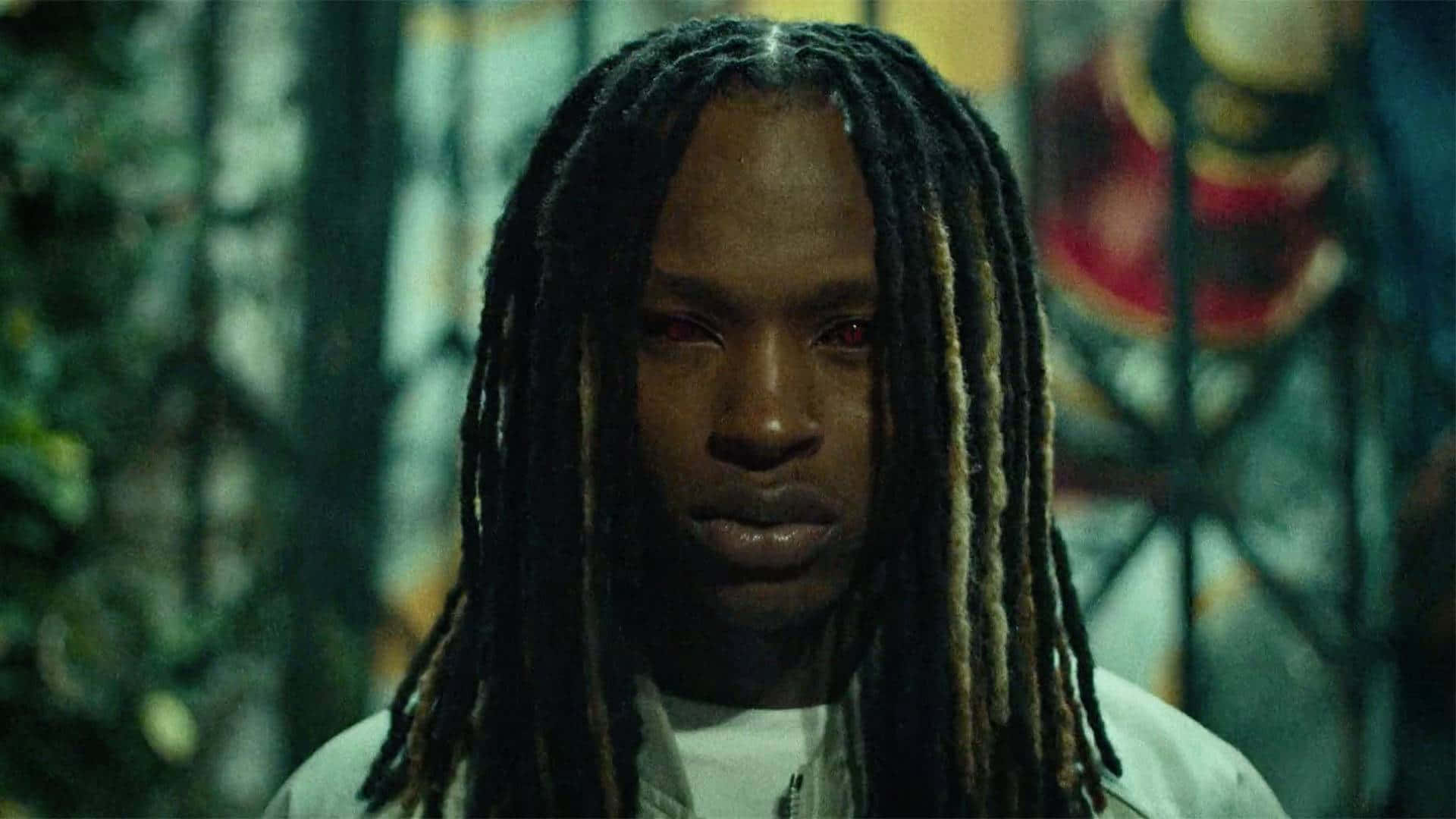 一個留著辮子的男人在粗獷的城市環境中直視鏡頭。 — King Von 壁紙