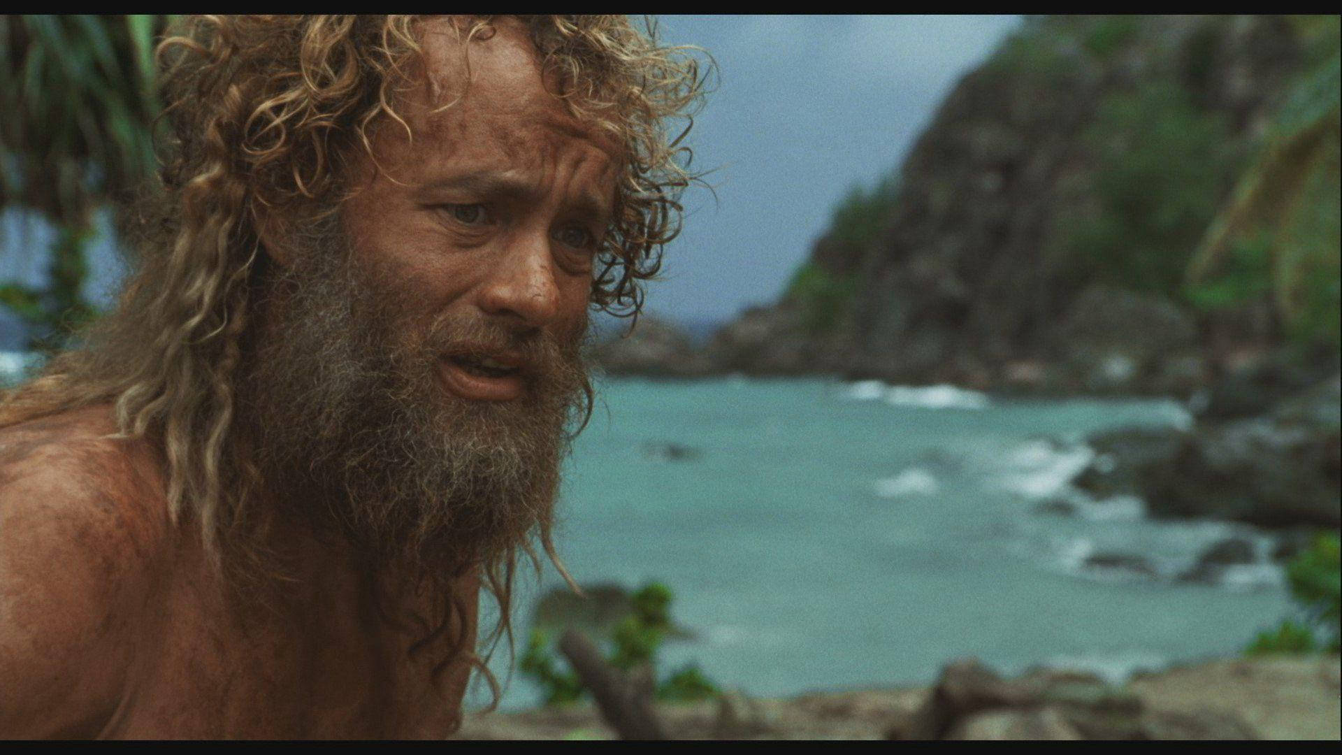 Tom 桌布 壁紙 — 一個留著鬍子、頭髮亂蓬蓬的男人，在碧綠的海洋和岩石峭壁的背景下凝視著。
