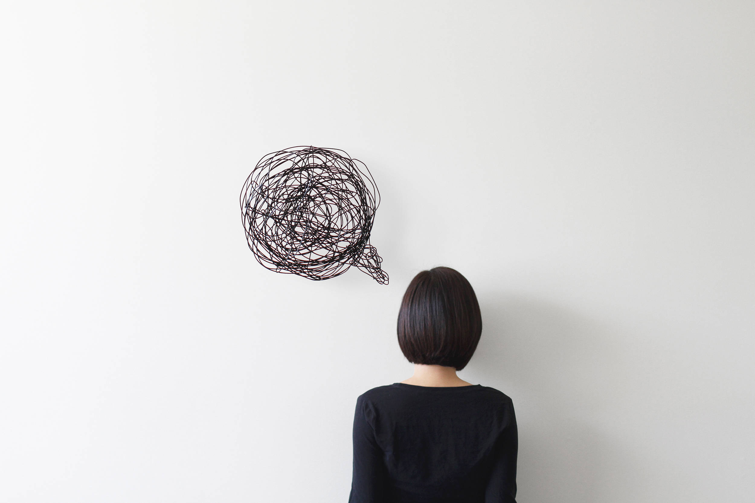 Anxiety 桌布 壁紙 — 一個留著鮑伯頭的人，凝視著安裝在純白牆上的一個纏結的黑色電線對話氣泡。