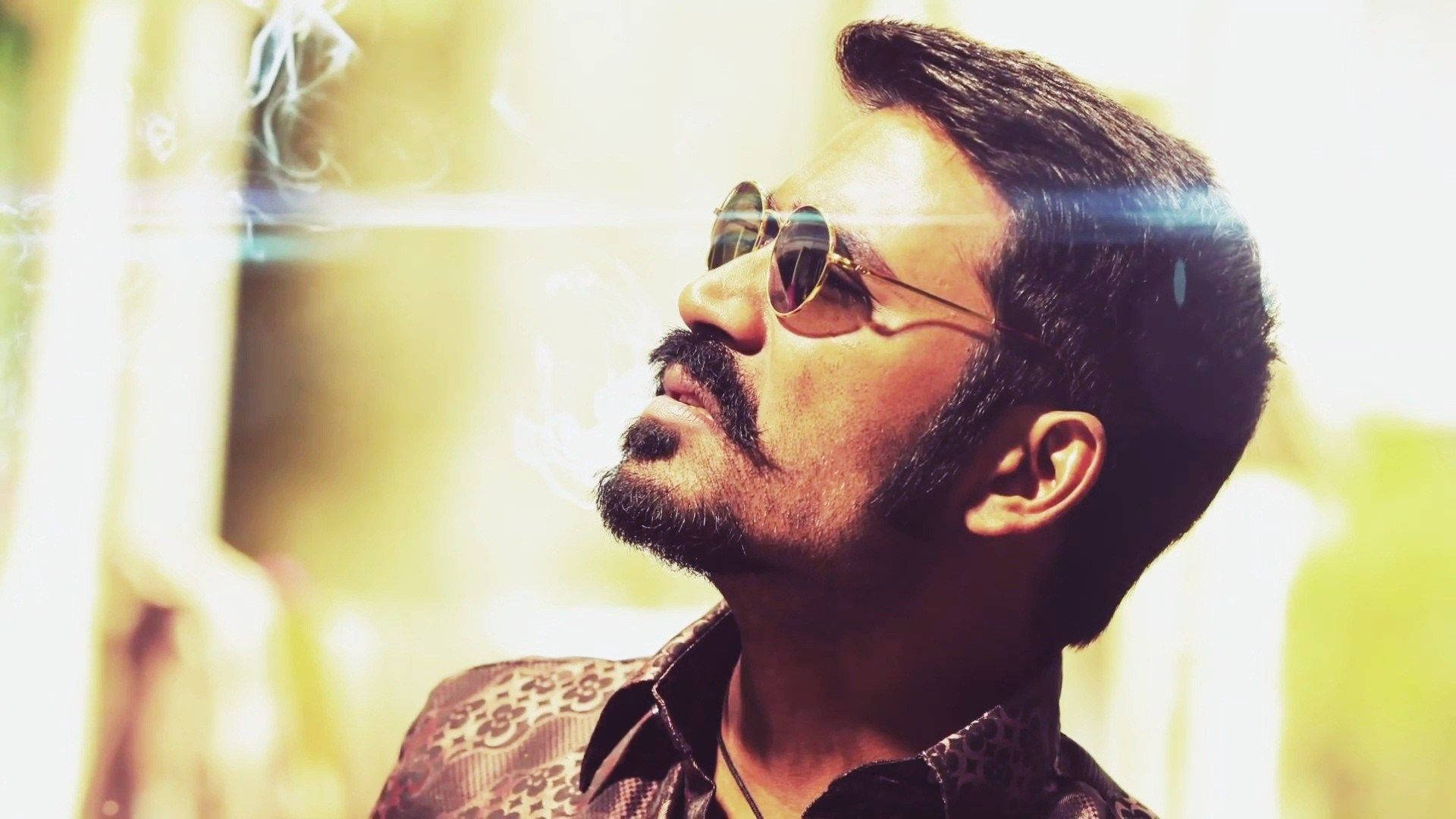 Bollywood HD 桌布 壁紙 — 一個留鬍子、戴太陽眼鏡的男人在明亮的金色背景和鏡頭光暈中呼出煙霧。
