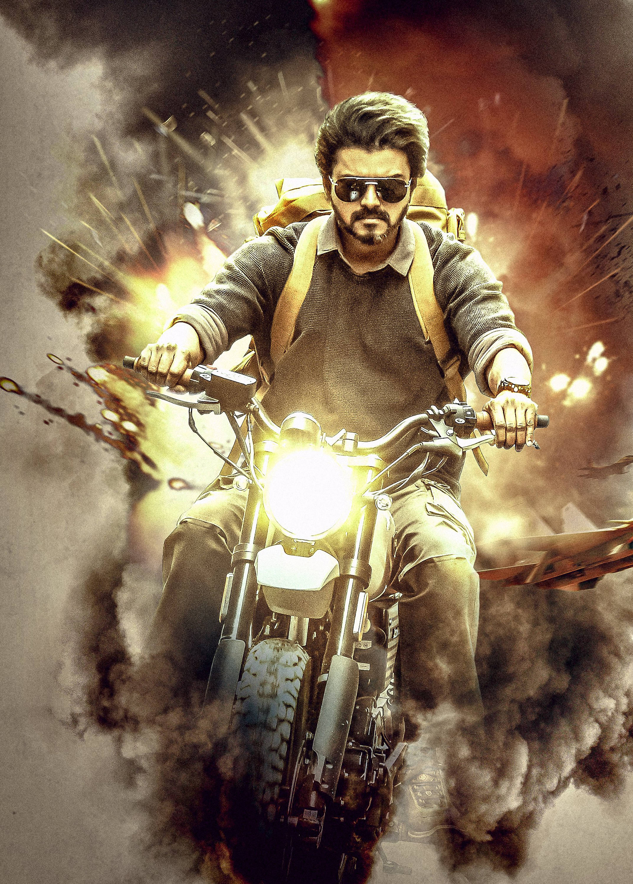 vijay HD 桌布 壁紙 — 一個留鬍子、戴太陽眼鏡的男人騎著機車穿過爆炸，周圍充滿煙霧和火焰。