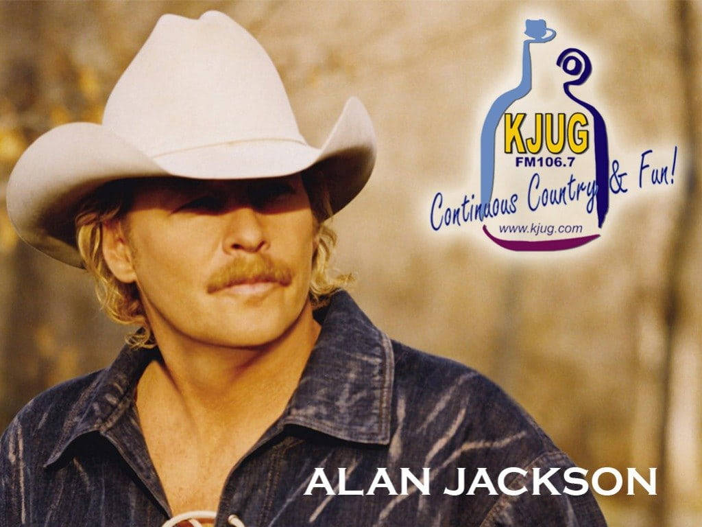 Alan Jackson 桌布 壁紙 — 一個留鬍子、戴牛仔帽的男人，在模糊的金色背景和電台品牌標誌前，視線離開鏡頭。