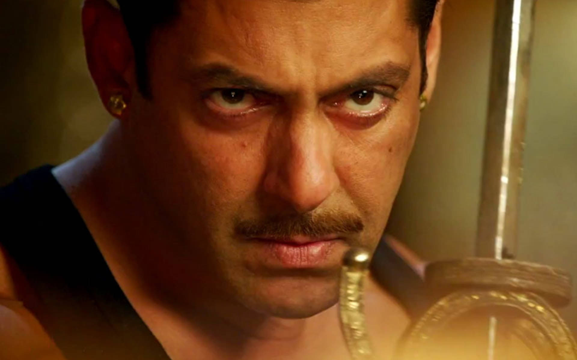 Salman Khan 桌布 壁紙 — 一個留鬍子、戴金耳環的男人，在溫暖的金色光芒中手持劍，眼神銳利。
