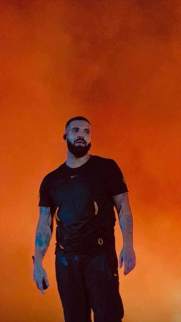 Drake 桌布 壁紙 — 一個留鬍子、有刺青的男人，自信地站在火橙色煙霧背景前，穿著黑色運動服。