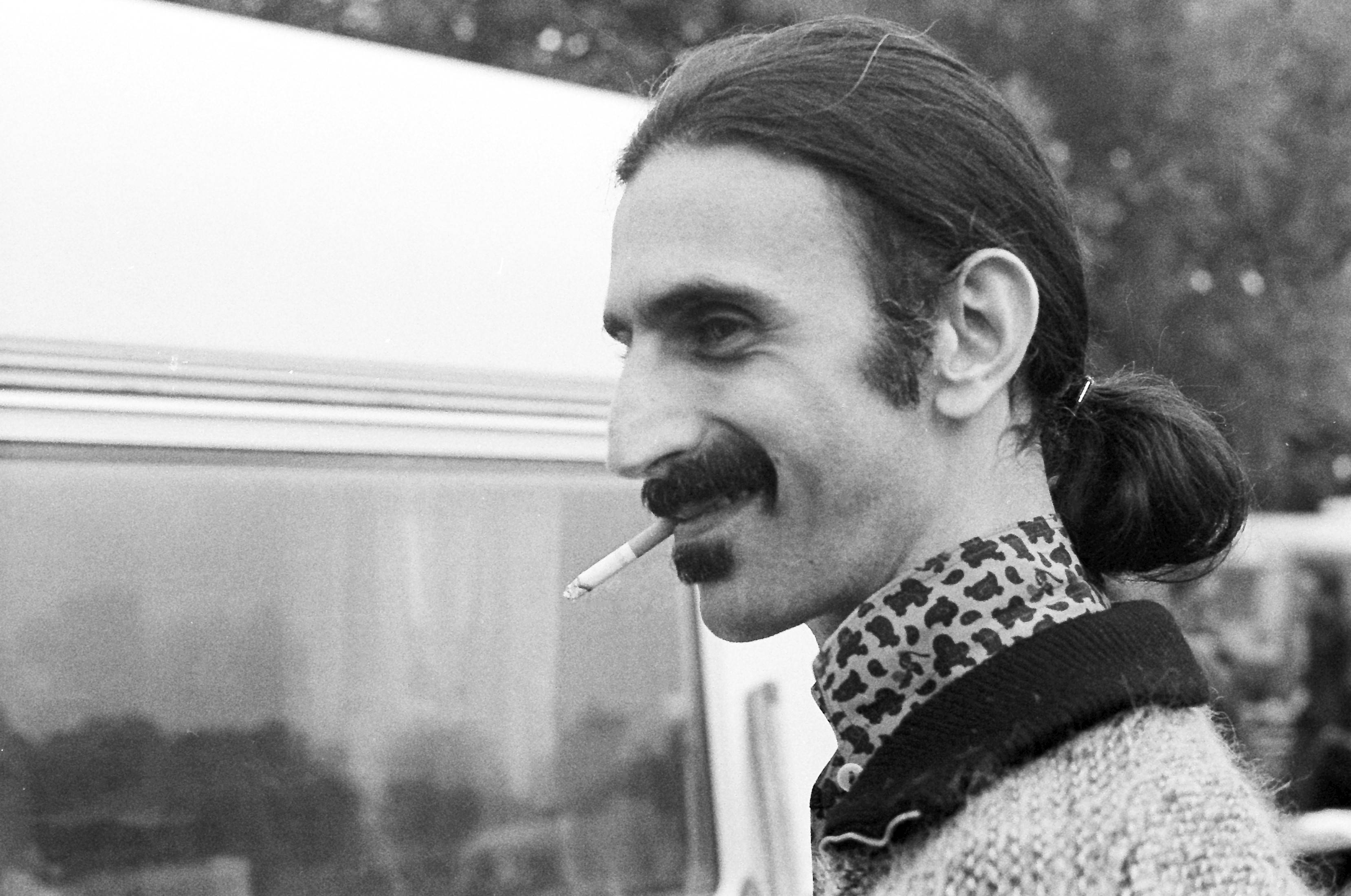 Zappa 桌布 壁紙 — 一個留鬍子、紮馬尾的男人在貨車附近抽煙的黑白肖像。