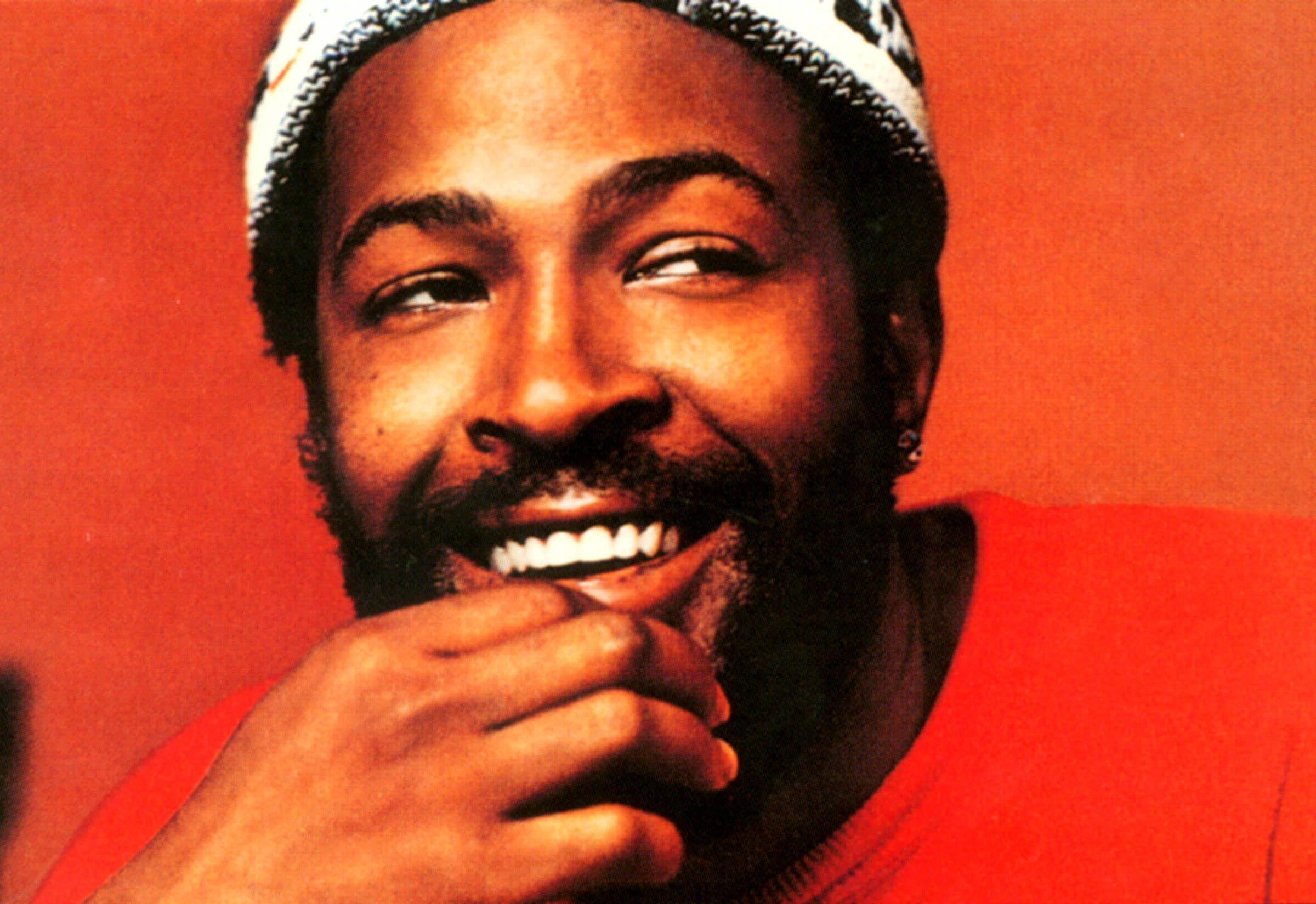 Marvin Gaye 桌布 壁紙 — 一個留鬍子戴毛帽的快樂男人，在溫暖的紅色背景上觸碰下巴，露出燦爛的笑容。