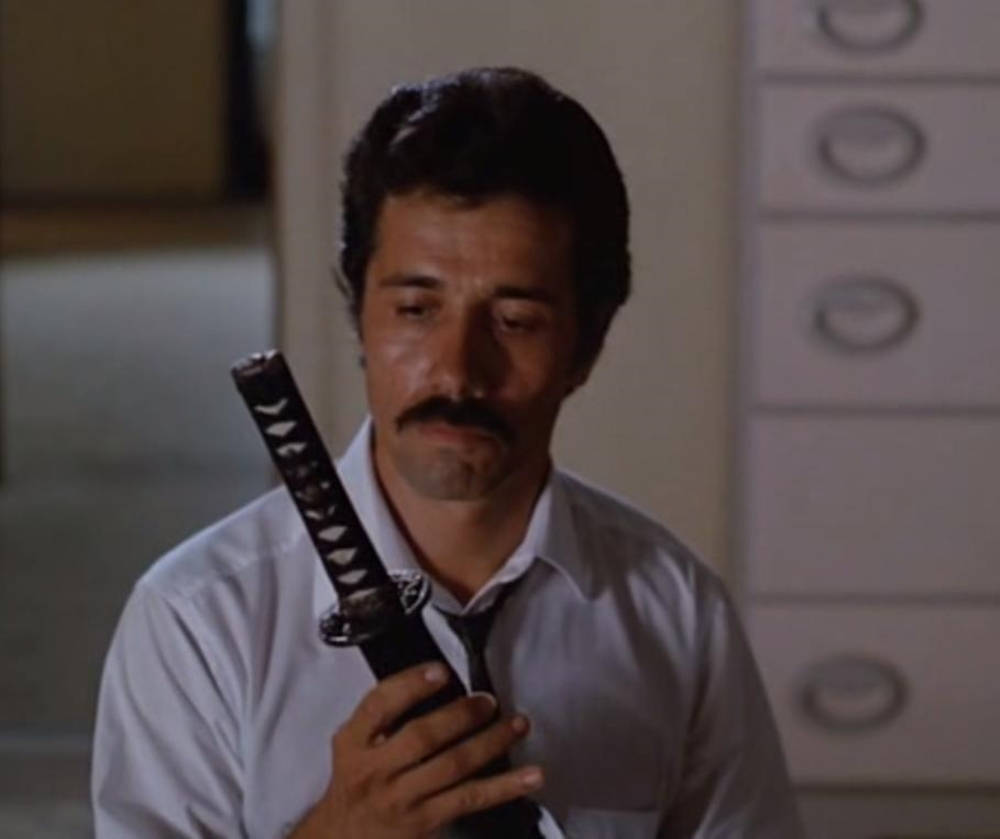 actor 桌布 壁紙 — 一個留鬍子的男人在燈光昏暗的辦公室裡拿著一把武士刀，身後有文件櫃。