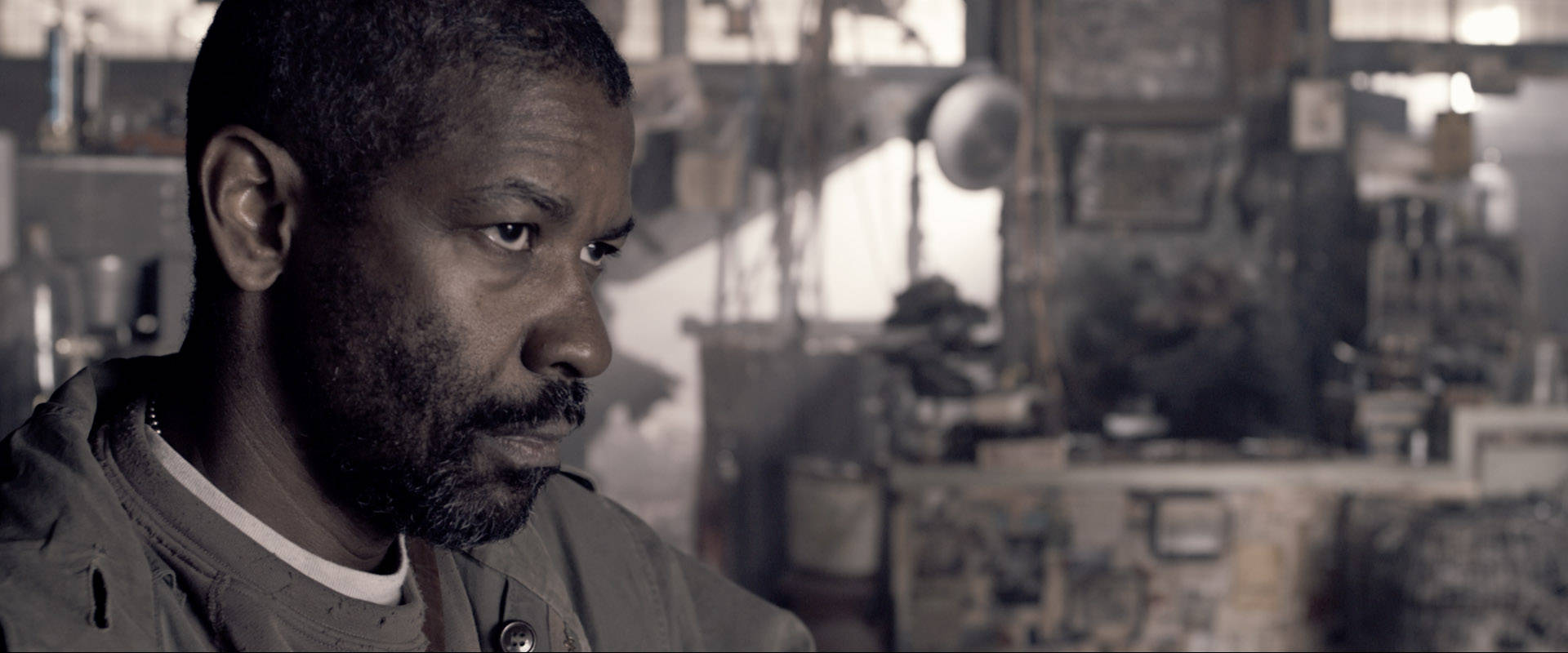 Denzel Washington 桌布 壁紙 — 一個留鬍子的男人在雜亂的工作室中，沐浴在柔和光線下，專注地凝視。