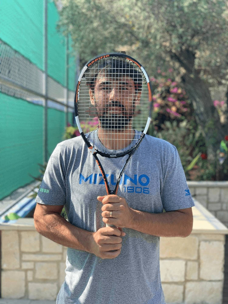 Tennis 桌布 壁紙 — 一個留鬍子的男人把網球拍舉到臉前，背景是綠色圍欄和開花的灌木叢。