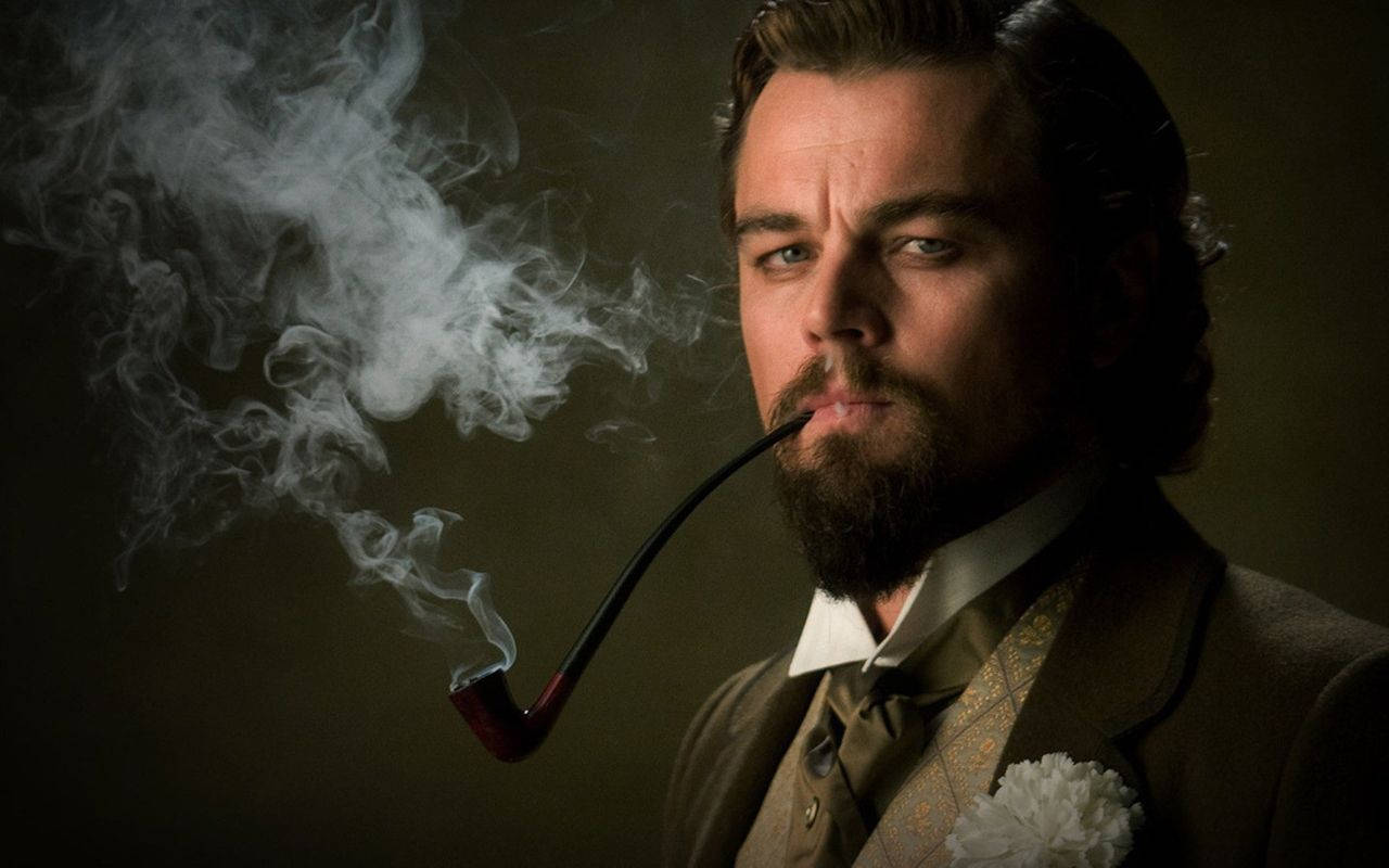 Dicaprio 桌布 壁紙 — 一個留鬍子的男人抽著煙斗，煙霧在黑暗背景中戲劇性地盤旋。