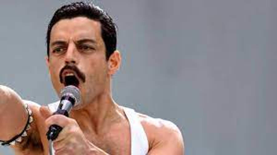 Rami Malek 桌布 壁紙 — 一個留鬍子的男人熱情地唱著麥克風，穿著白色背心和珠子手鍊。