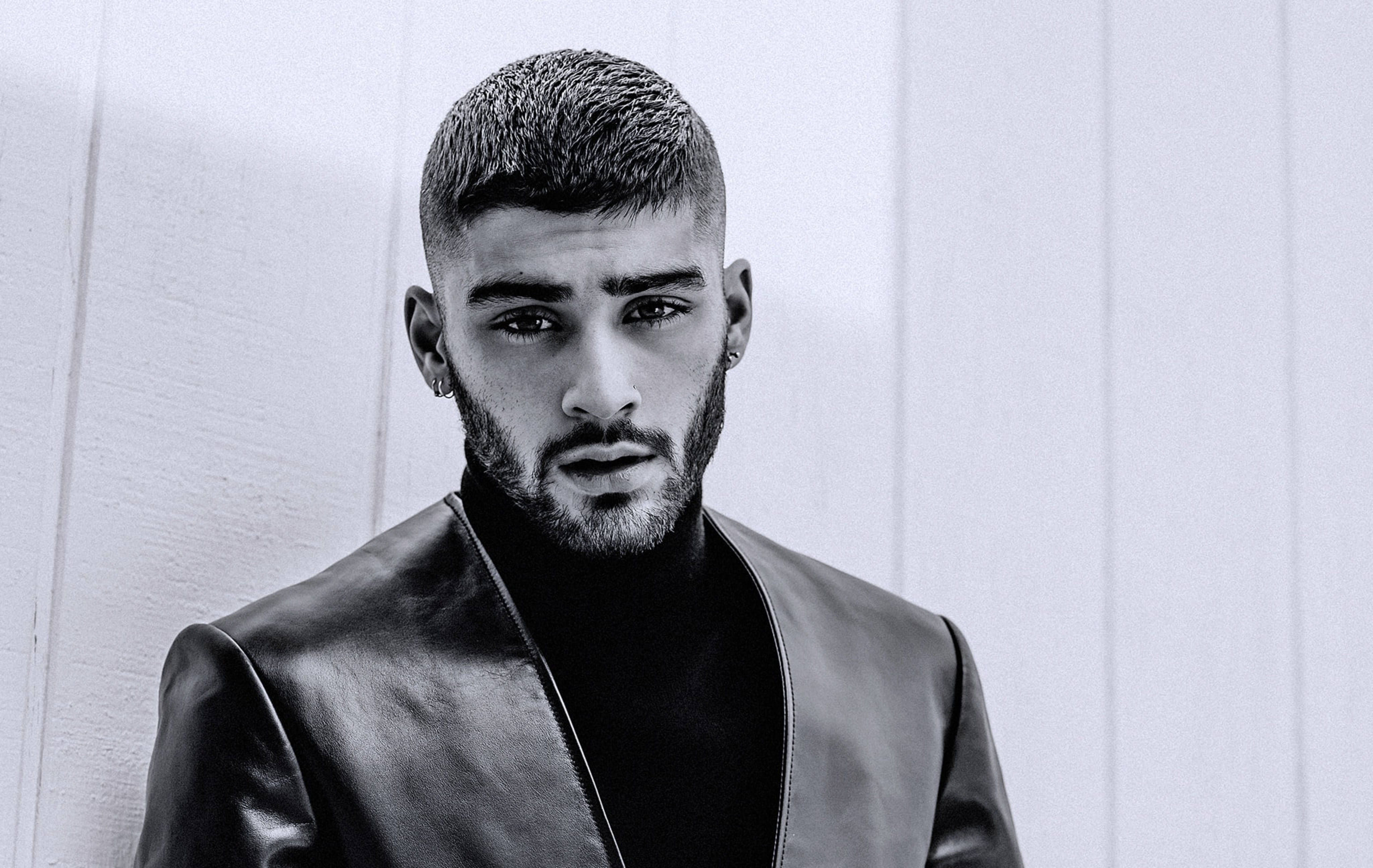 zayn 桌布 壁紙 — 一個留鬍子的男人穿著皮夾克靠著素面牆壁的黑白肖像。